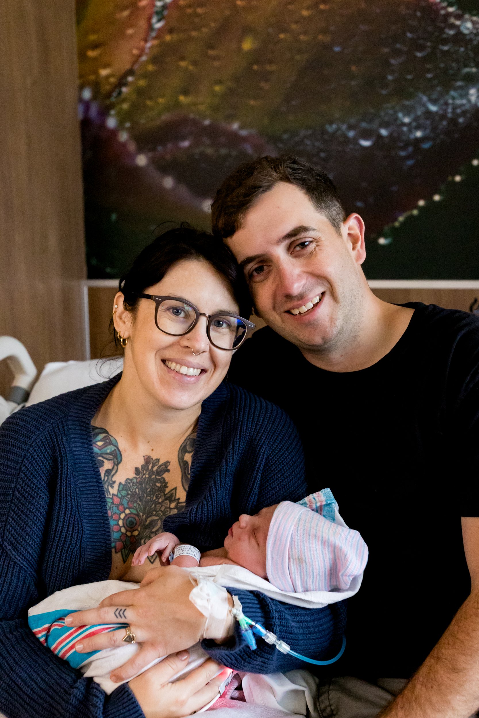 couple smiling at the camera while holding newborn baby