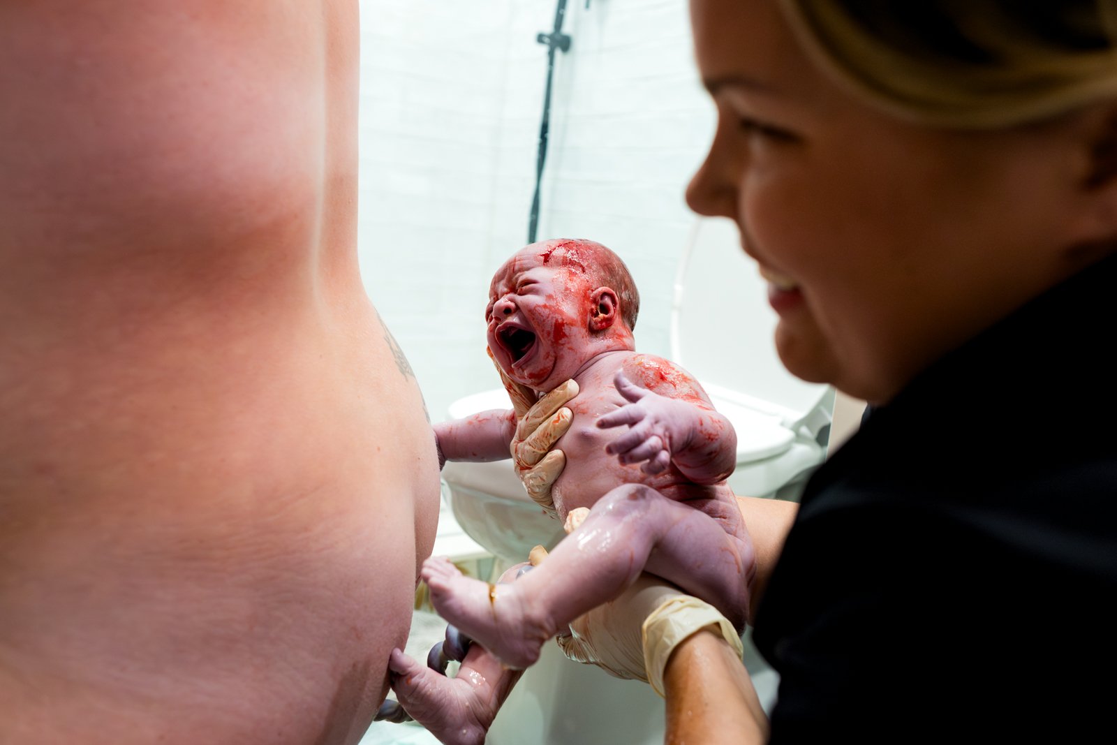 midwife holding up crying newborn baby just after birth