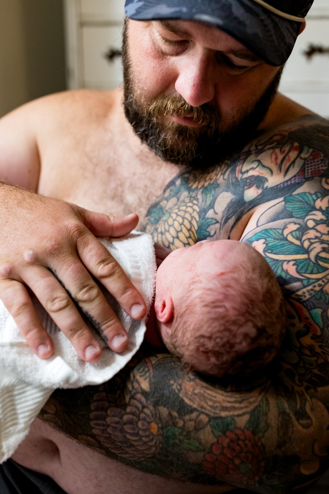 new dad gazing at his newborn baby girl while he holds her close to his chest