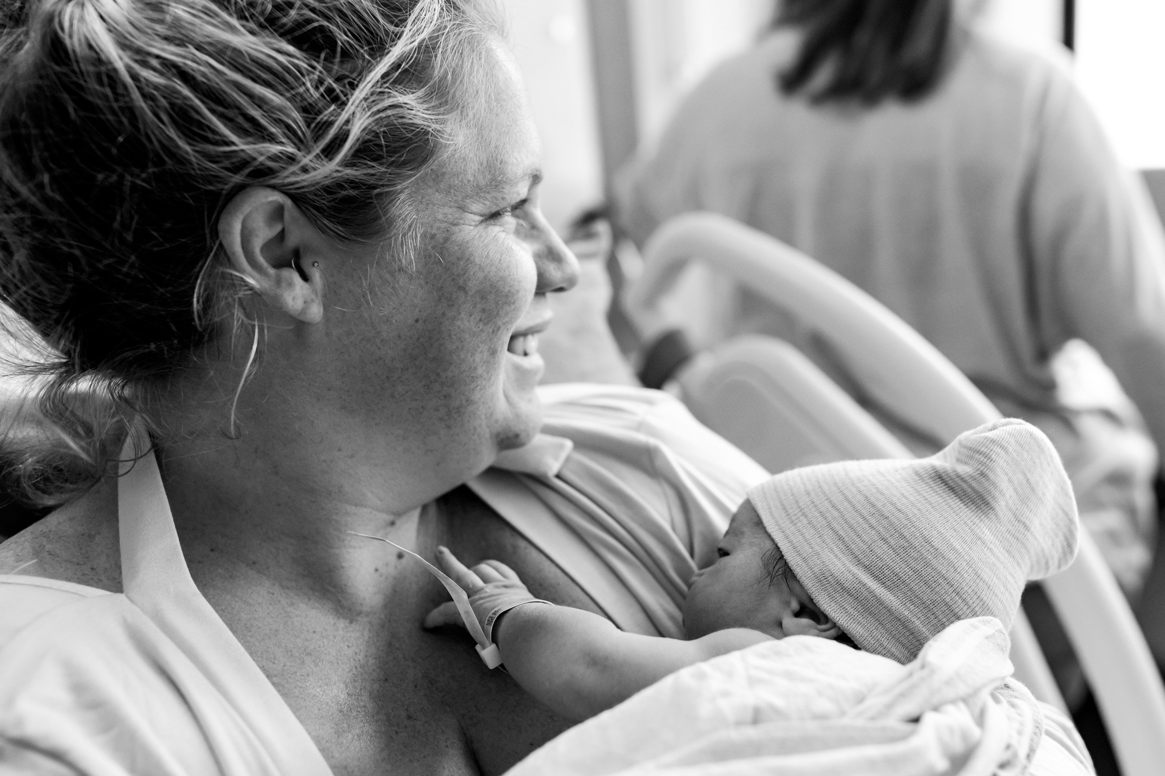 mom smiling and looking off into the distance as she holds her newborn baby girl