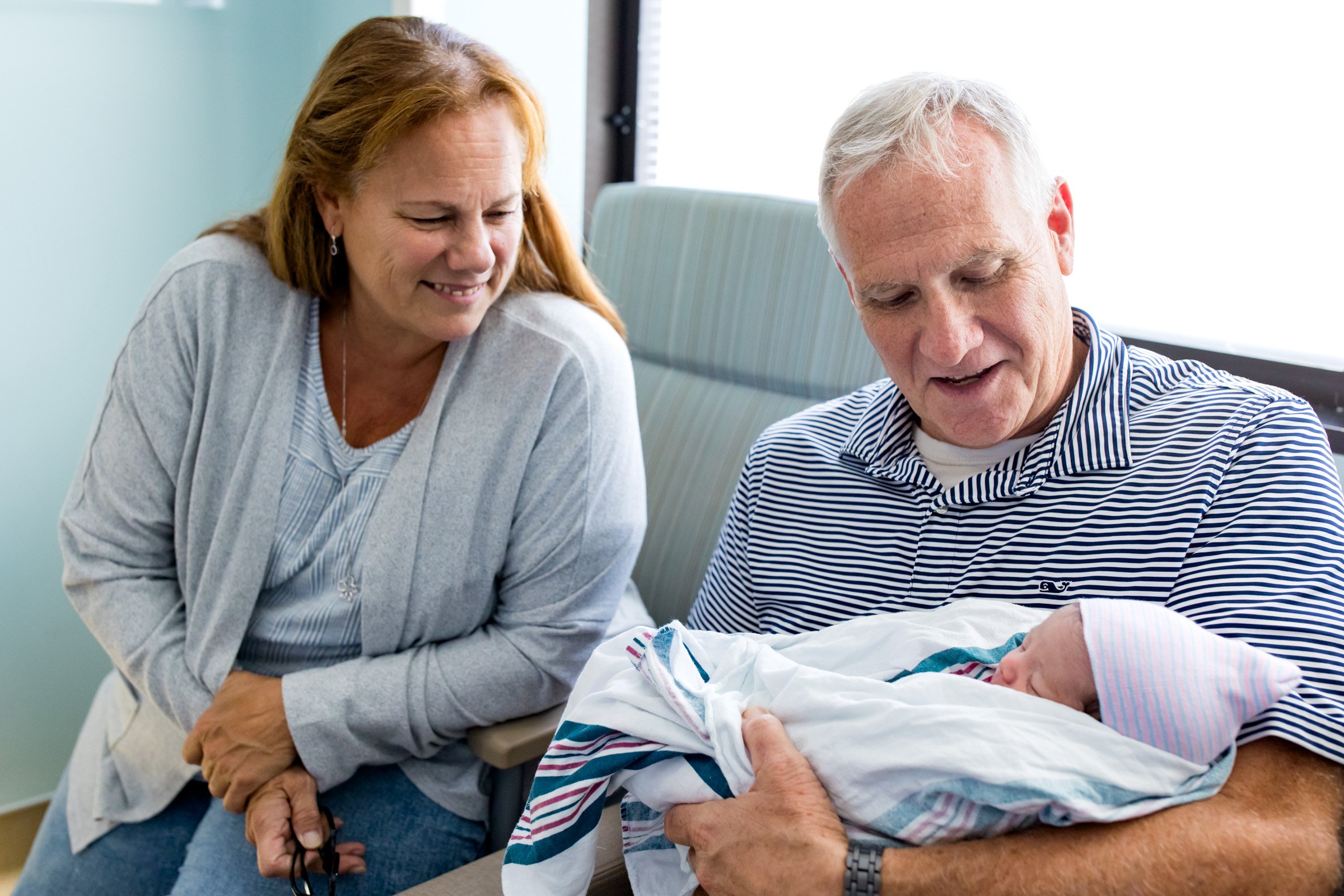 grandparents smiling as they hold baby granddaughter just after birth