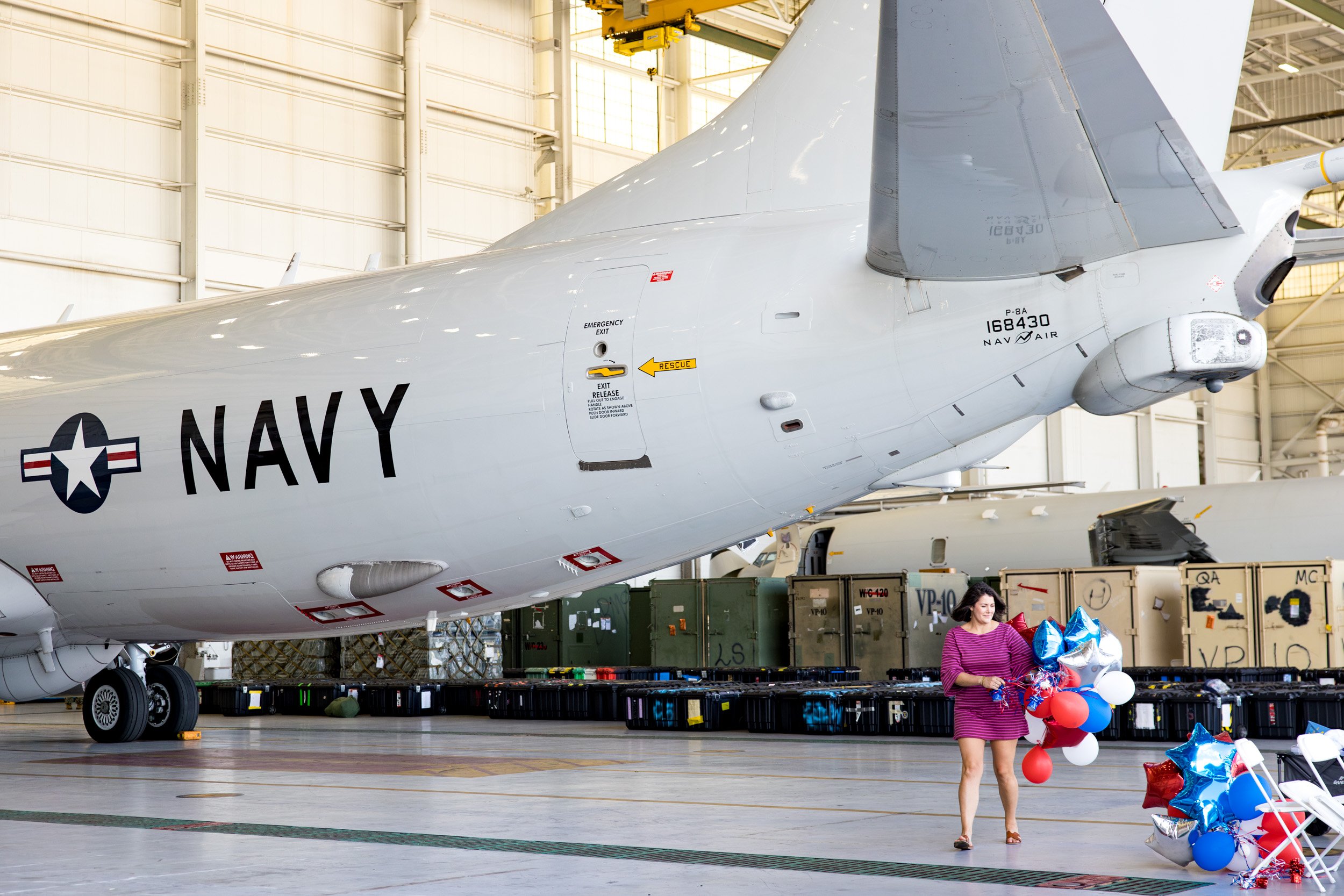 Navy pilot wife carrying red, white, and blue balloons next to plane in hangar