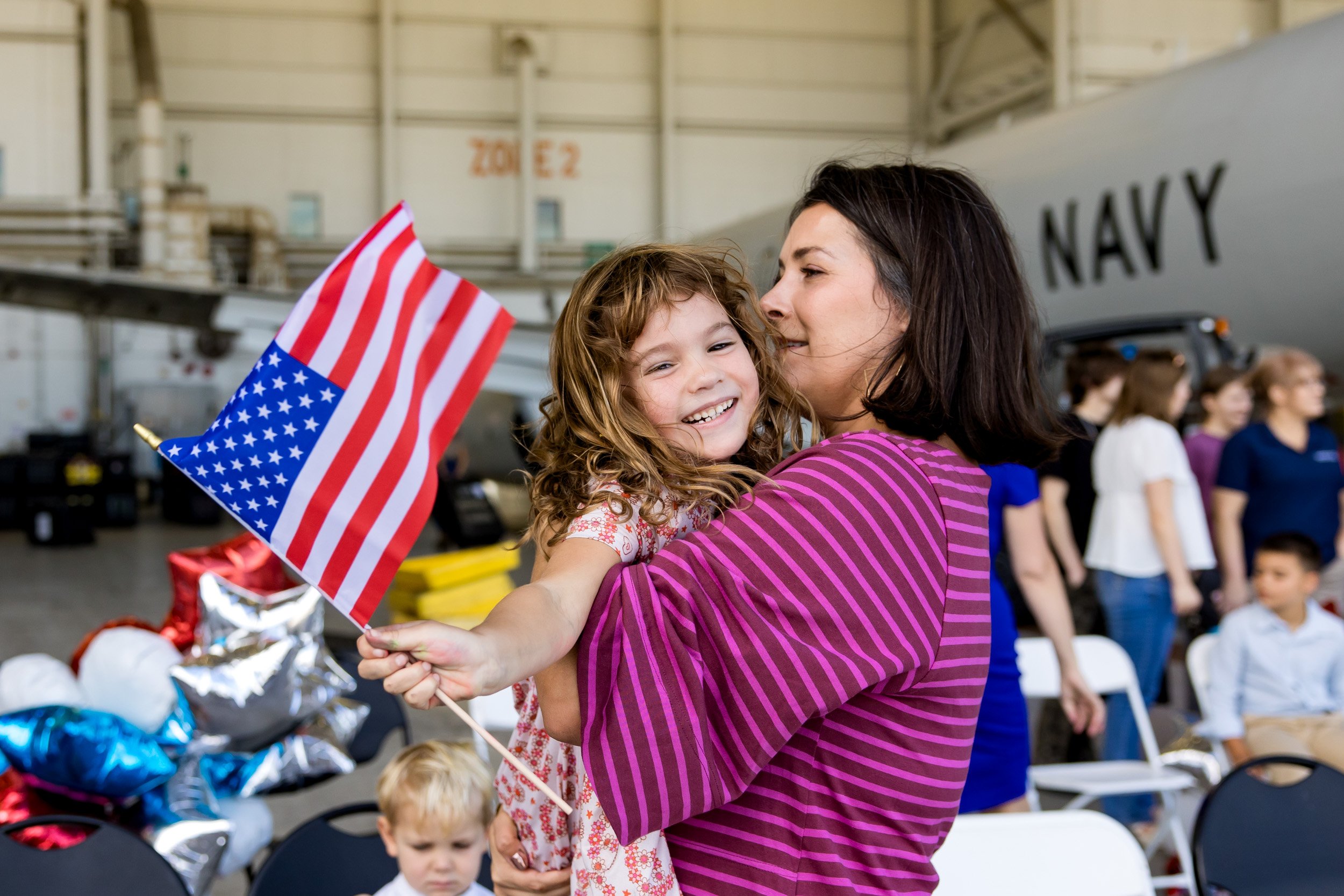 little girl holding an American flag while smiling and being held by her mom