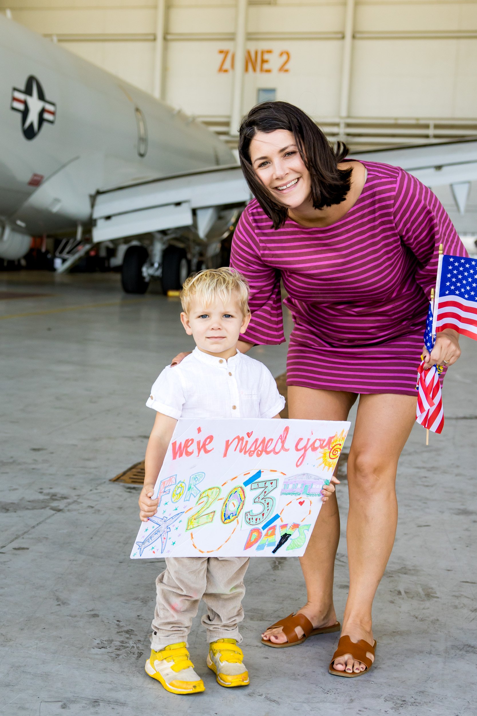 mom and little boy holding up a sign for dad while waiting for him to arrive after deployment