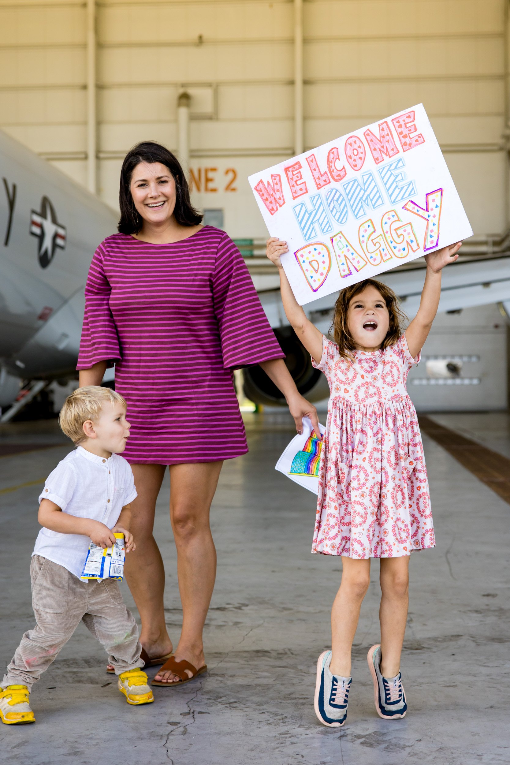 family holding up a sign for dad while waiting for him to arrive after deployment