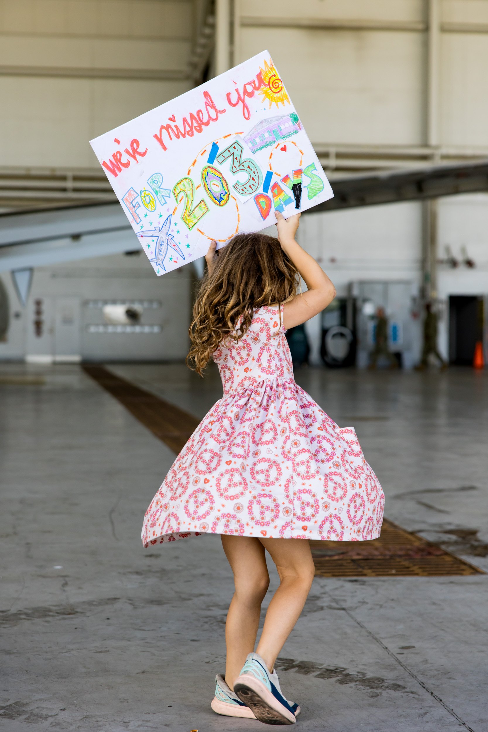 little girl holding up a sign for dad while waiting for him to arrive after deployment