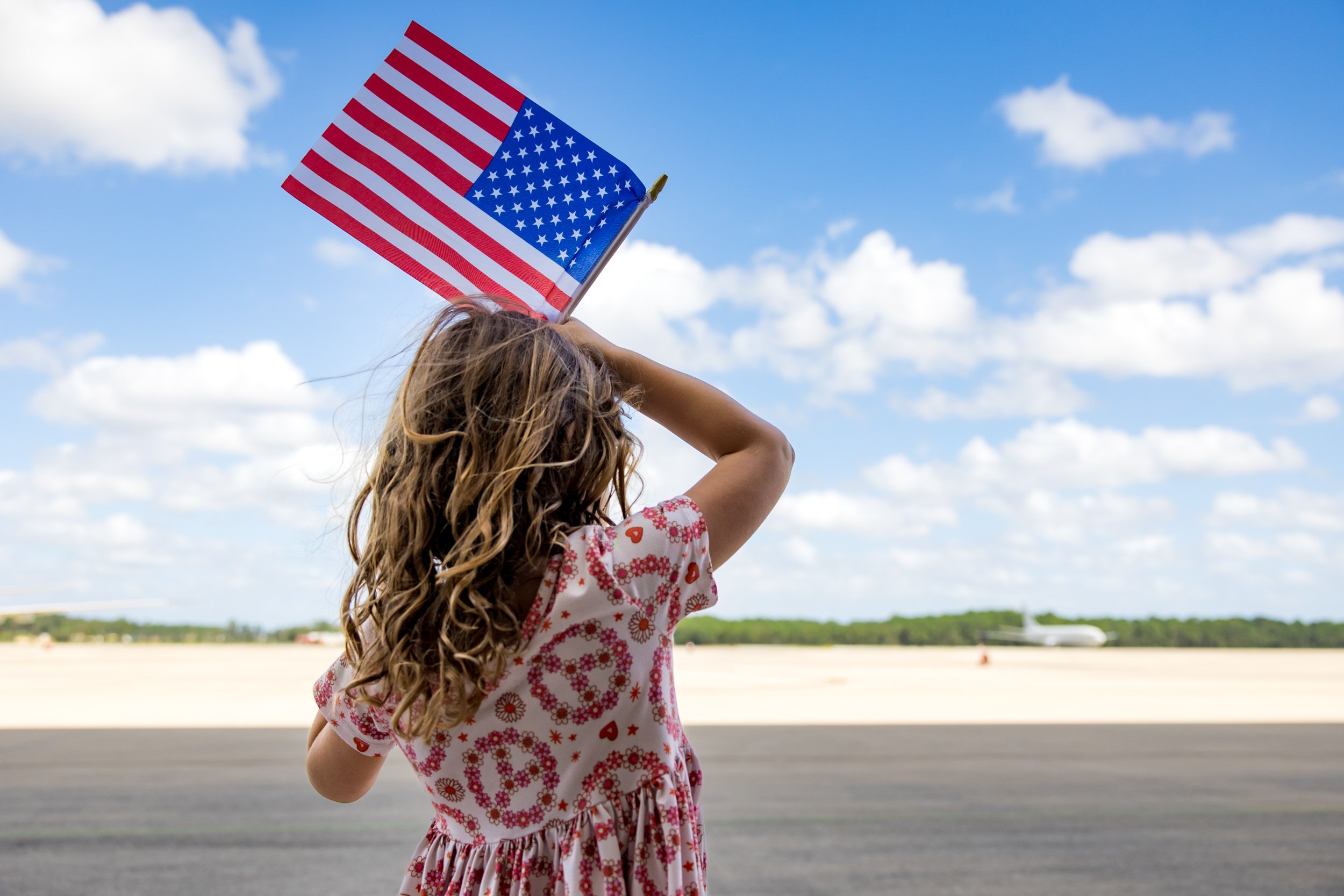 little girl holding up American flag as she watches her dad's plane taxi on the runway