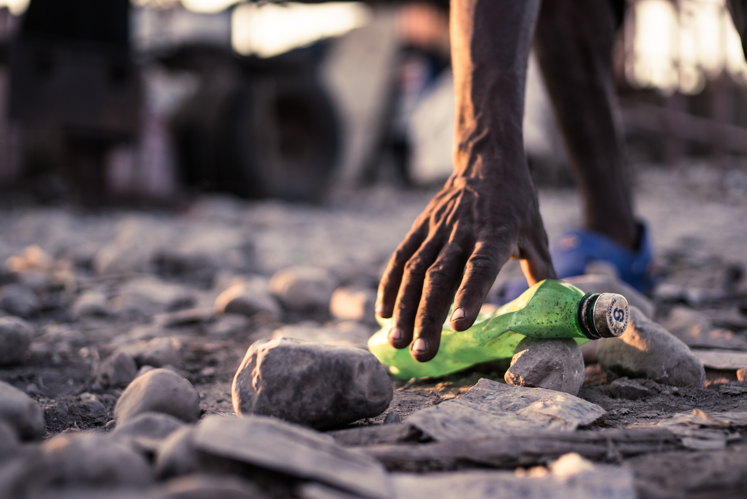 Collector picking up a bottle of the streets of Les Cayes.
