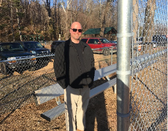 Photo of man standing against a chainlink baseball fence