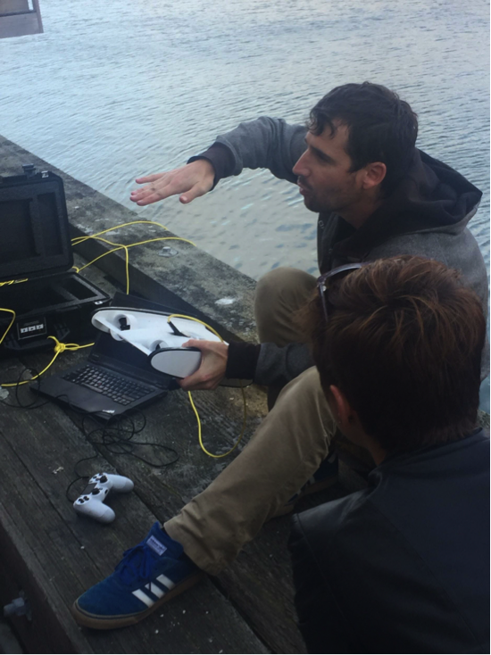 Eric Stackpole of OpenROV with their latest design, the Trident, in San Francisco March 2017. Note the game controller and the laptop, which displays tele-robotic views of what lies beneath the pier. © Jennie Rose (used with permission)