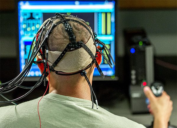 A test subject at the US Airforce's Non-Invasive Brain Stimulation lab uses a controller to navigate a set of computer tasks. Electrodes for targeted brain stimulation are attached to his head. J.M. Eddins, Jr./US Air Force (CC BY 2.0)