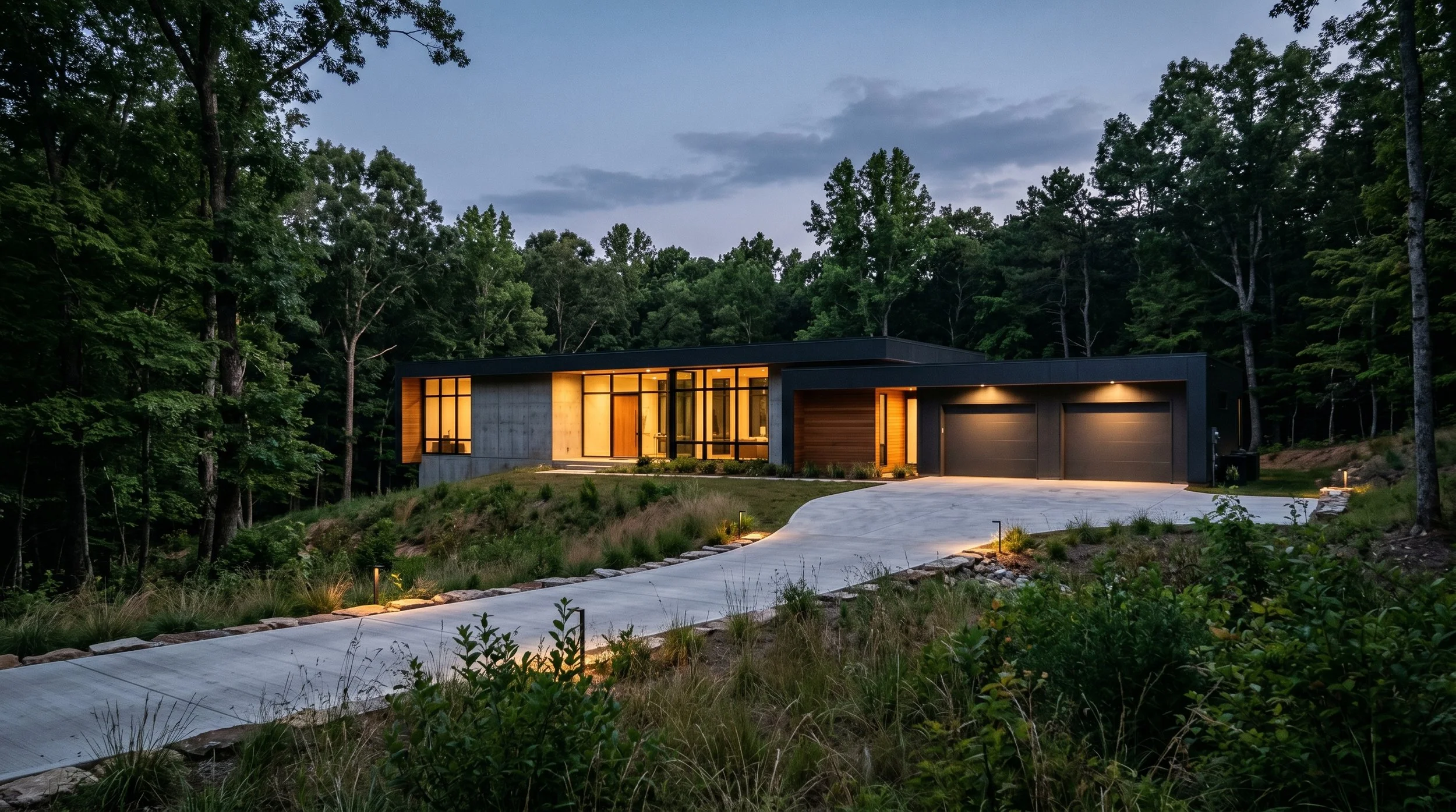 Modern house with large glass windows, situated in a wooded area, illuminated from inside at dusk.