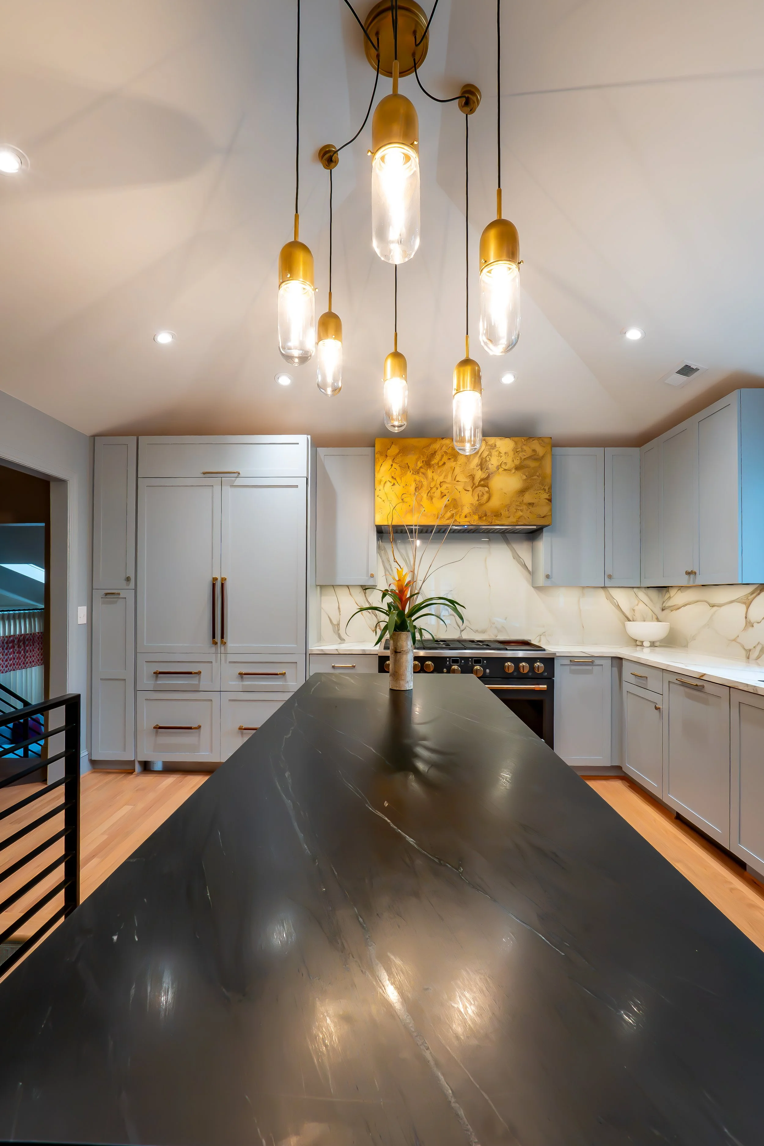Modern kitchen with white cabinets, a black marble kitchen island, a gold and glass chandelier, a plant, and a marble backsplash.
