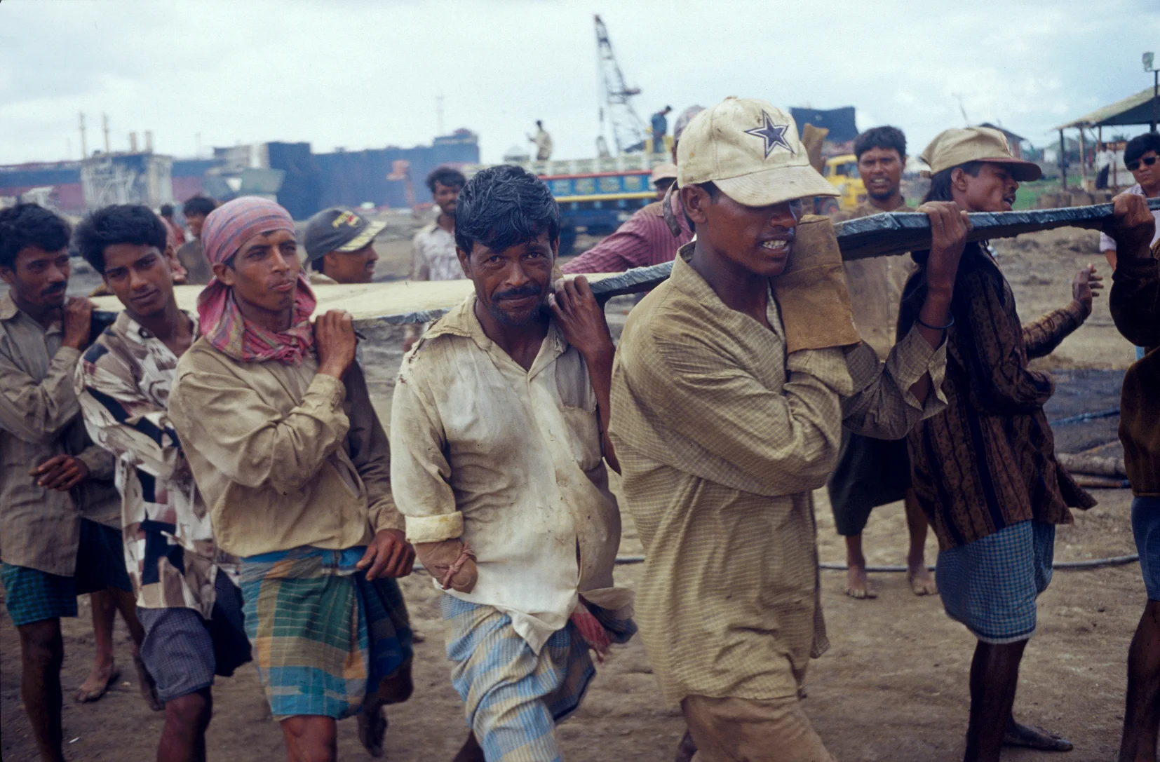 Workers on shipbreaking yards carry heavy pieces of steel scrapped from ships