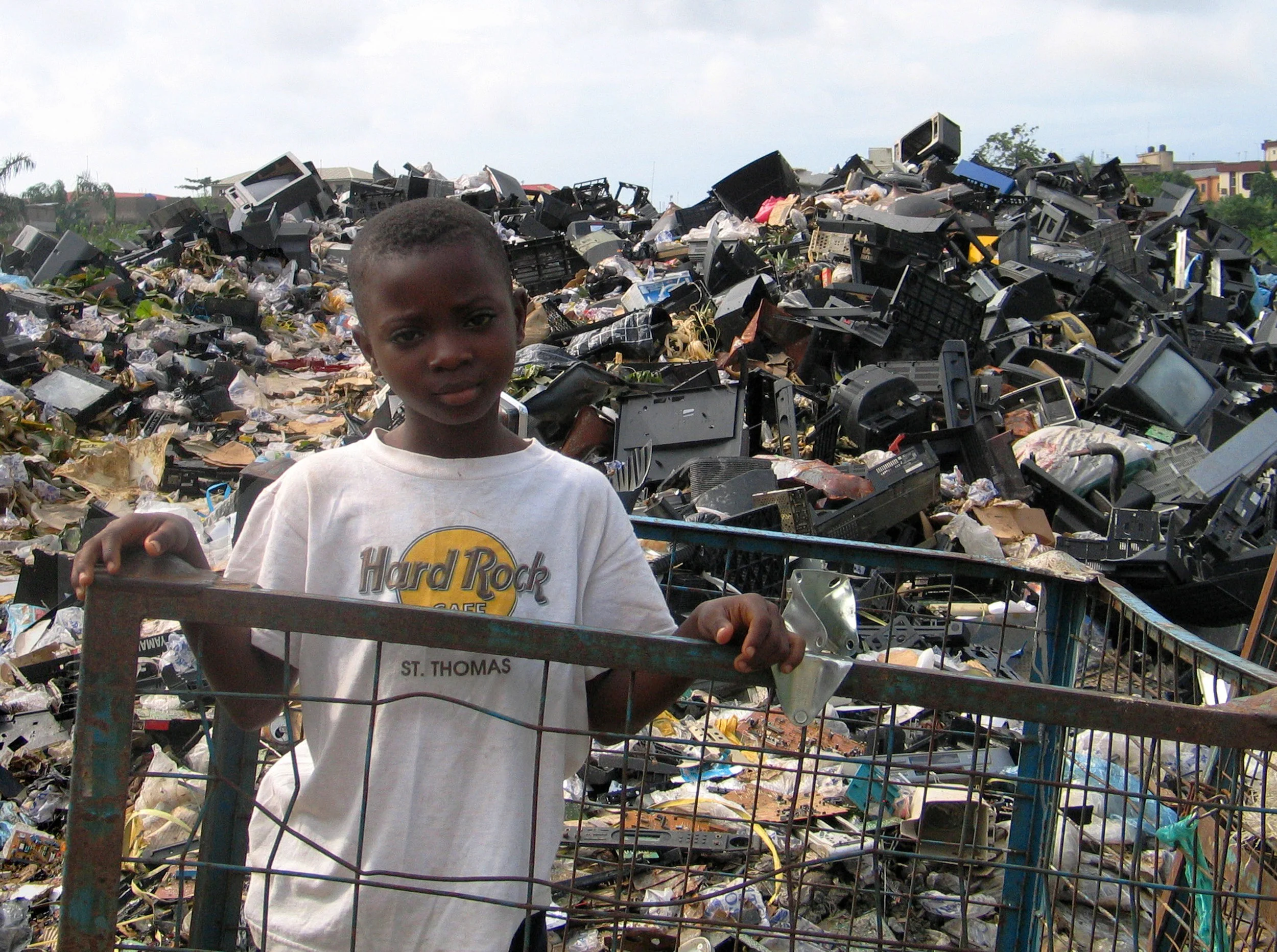 Market scavenger at electronic waste dump of unrepairable, unusable imported e-waste from North America and Europe. Such dumps are set ablaze routinely resulting in highly toxic air emissions. Alaba market, Lagos, Nigeria. Copyright Basel Action Network 2005.
