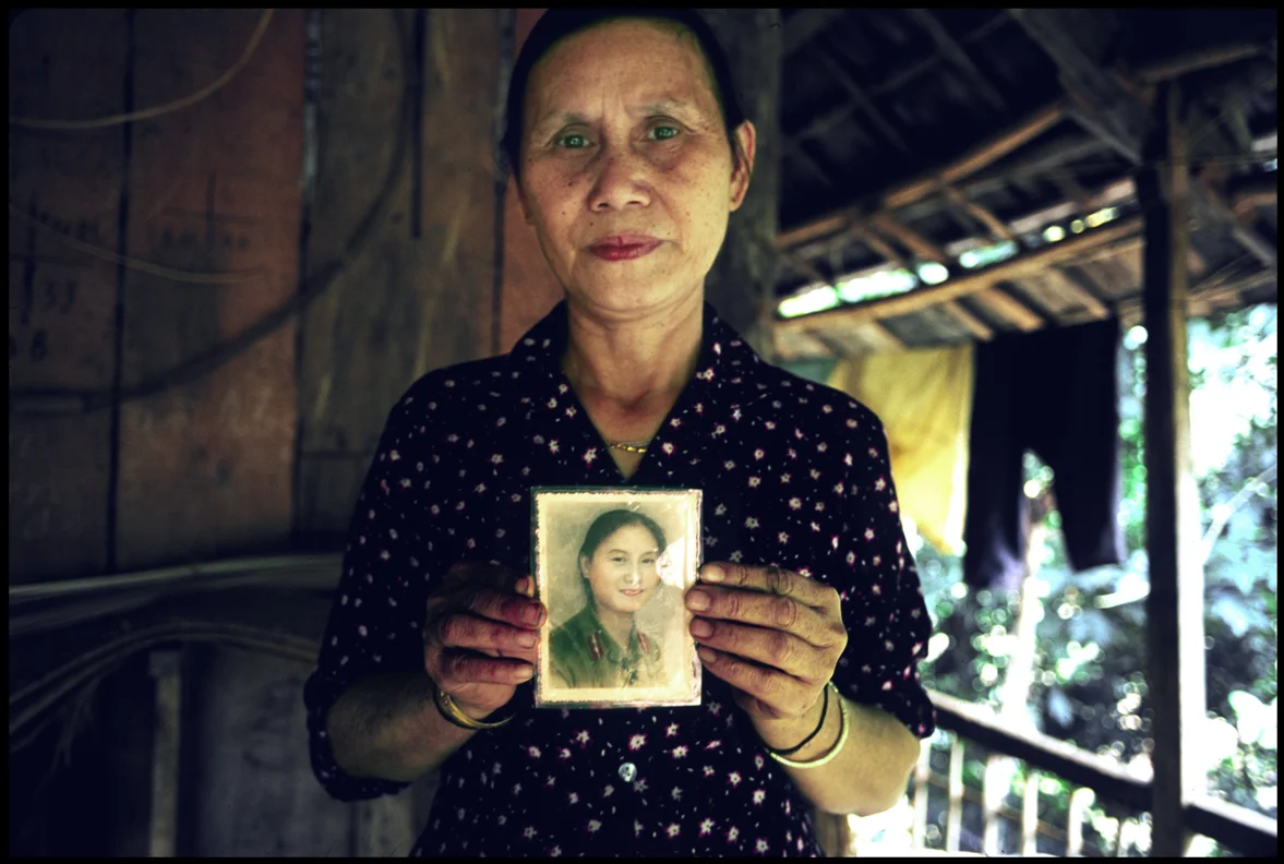 Portrait of villager holding up photograph of her young self.