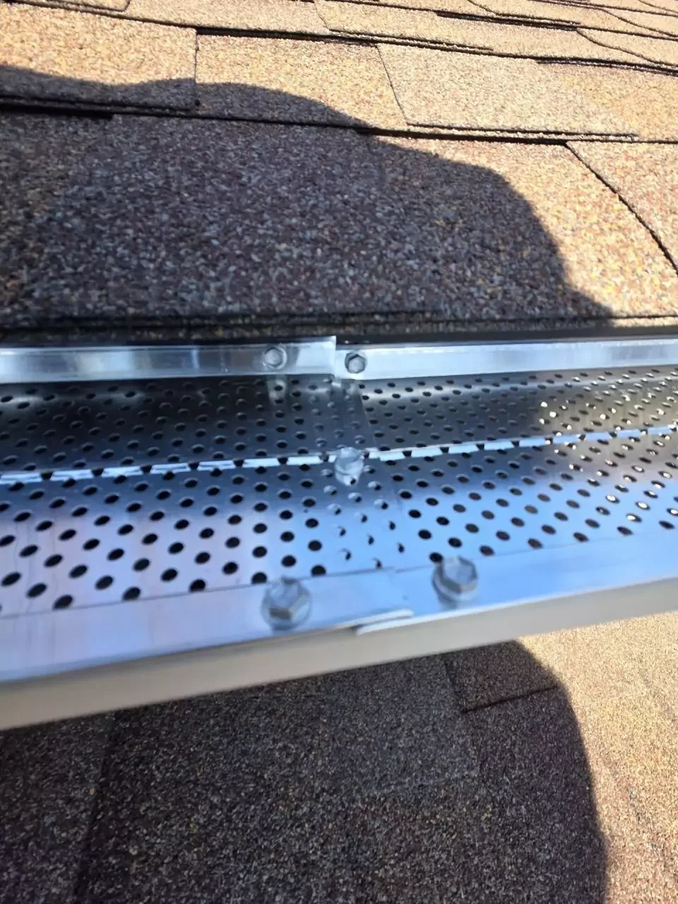 A close up view of a stainless steel micro-mesh gutter guard system installed on a residential roof.