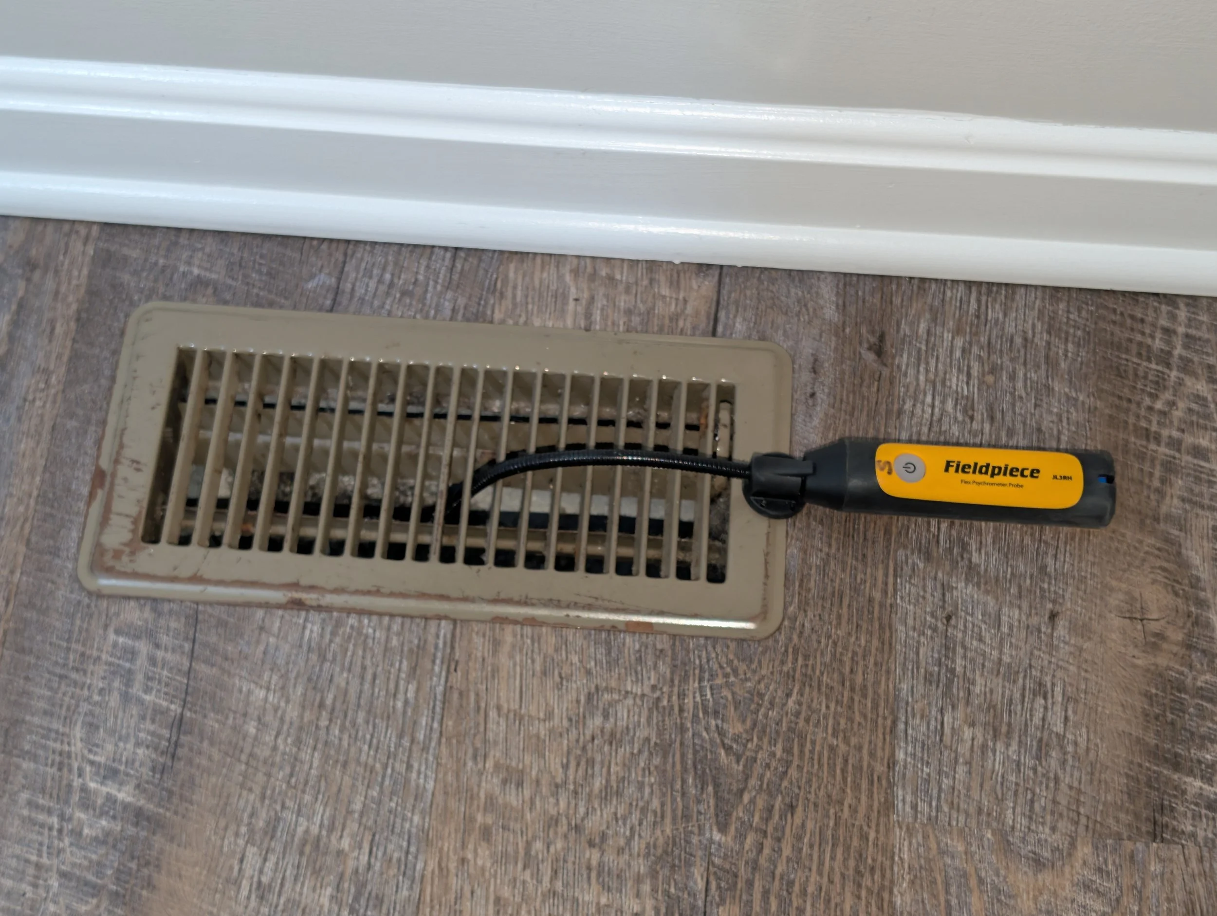 1st American Home Inspections using a Fieldpiece digital psychrometer to measure air temperature at a supply register for an HVAC thermal loss evaluation in Maryland.