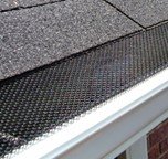 A close-up view of a black metal screen gutter guard installed on a residential roof line.