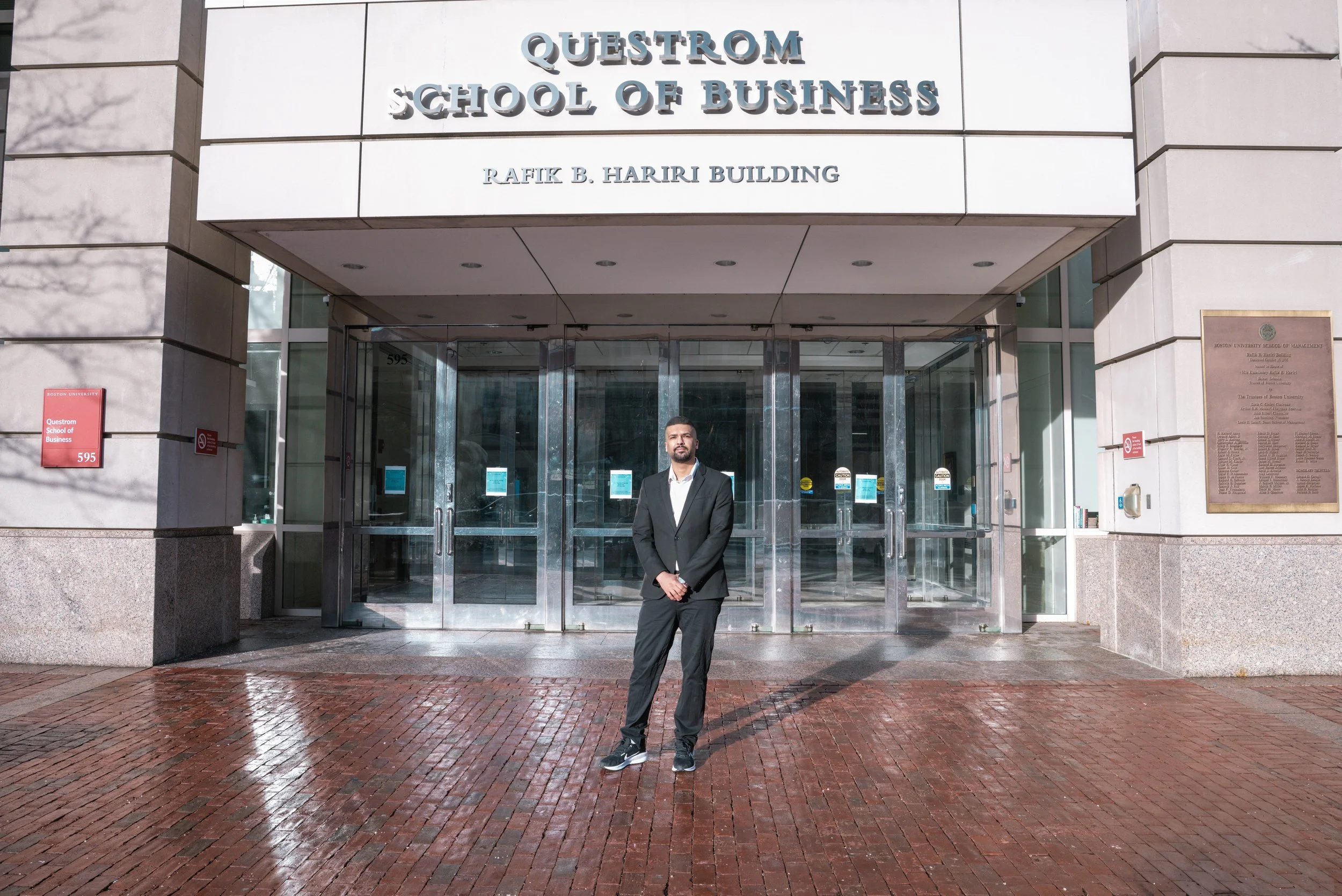Person standing in front of the QuESTROM School of Business entrance at Rafik B. Hariri Building, with glass doors and a plaque on the wall.