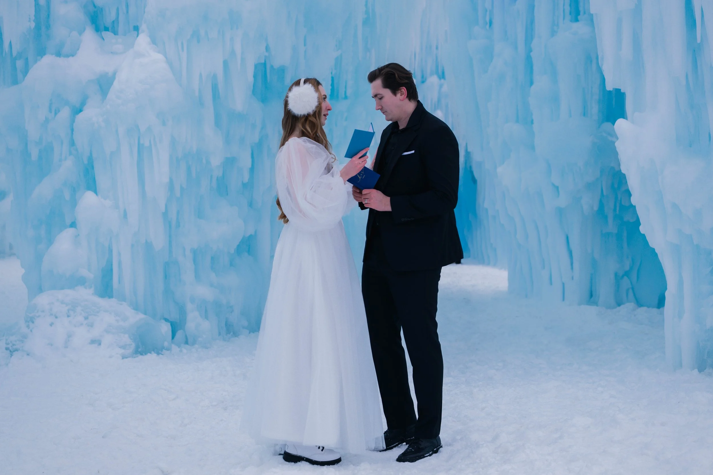 A couple wearing wedding attire exchanging vows inside an ice castle.