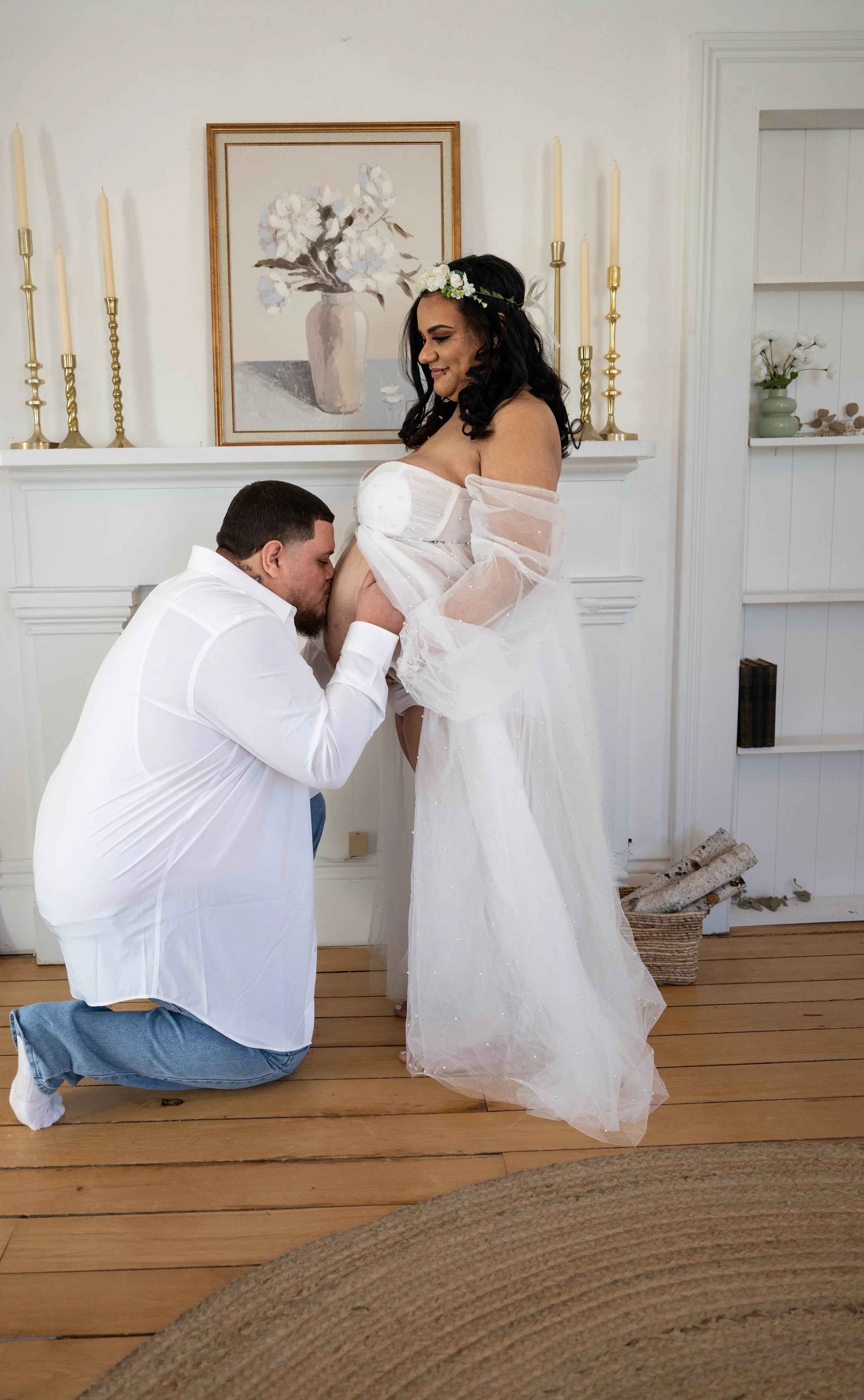 A man kneeling and kissing a pregnant woman's belly in a cozy, decorated room.