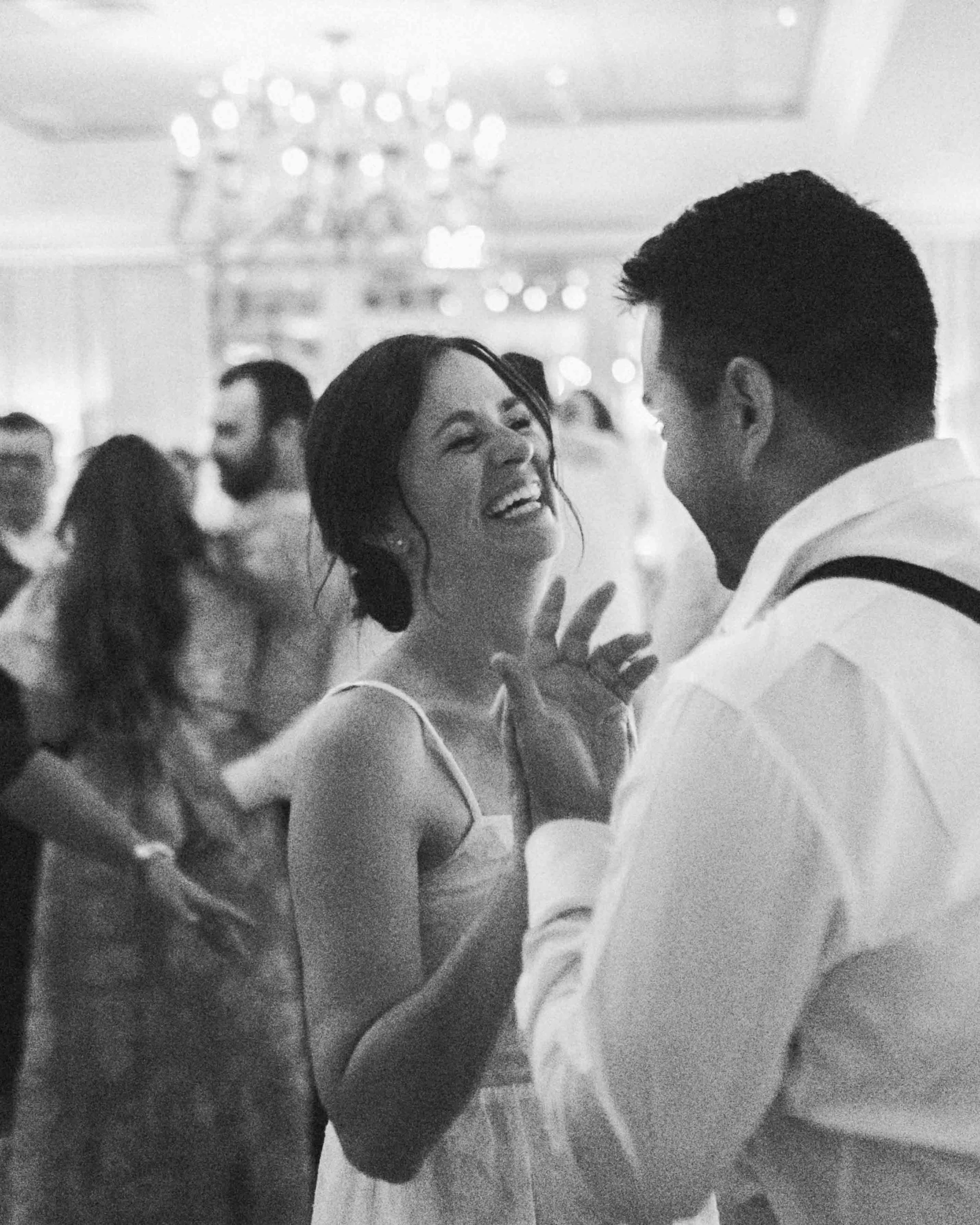 Bride and groom laughing together on the dance floor in black and white.