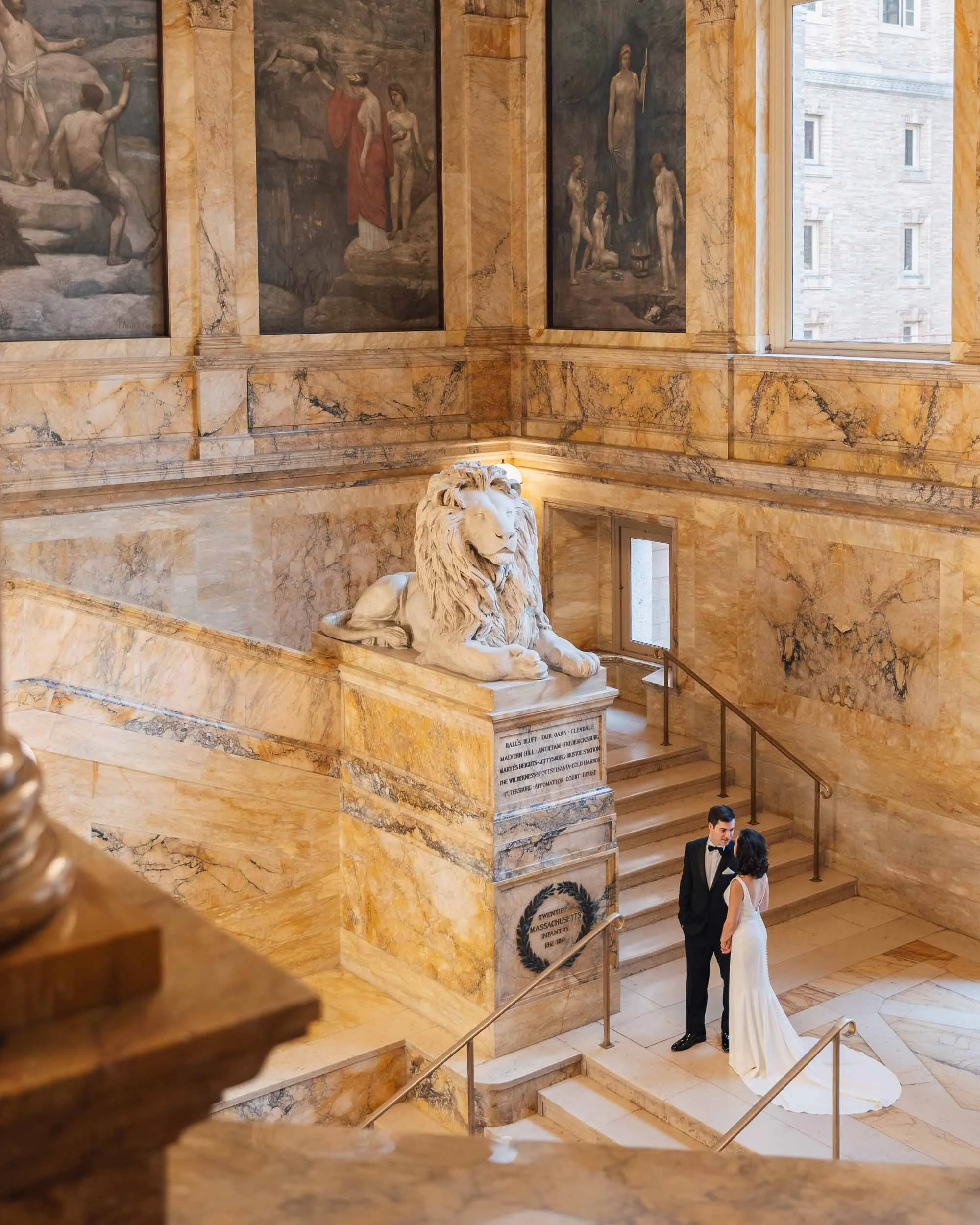 Grand marble staircase and lion statue inside the library, couple at the base.
