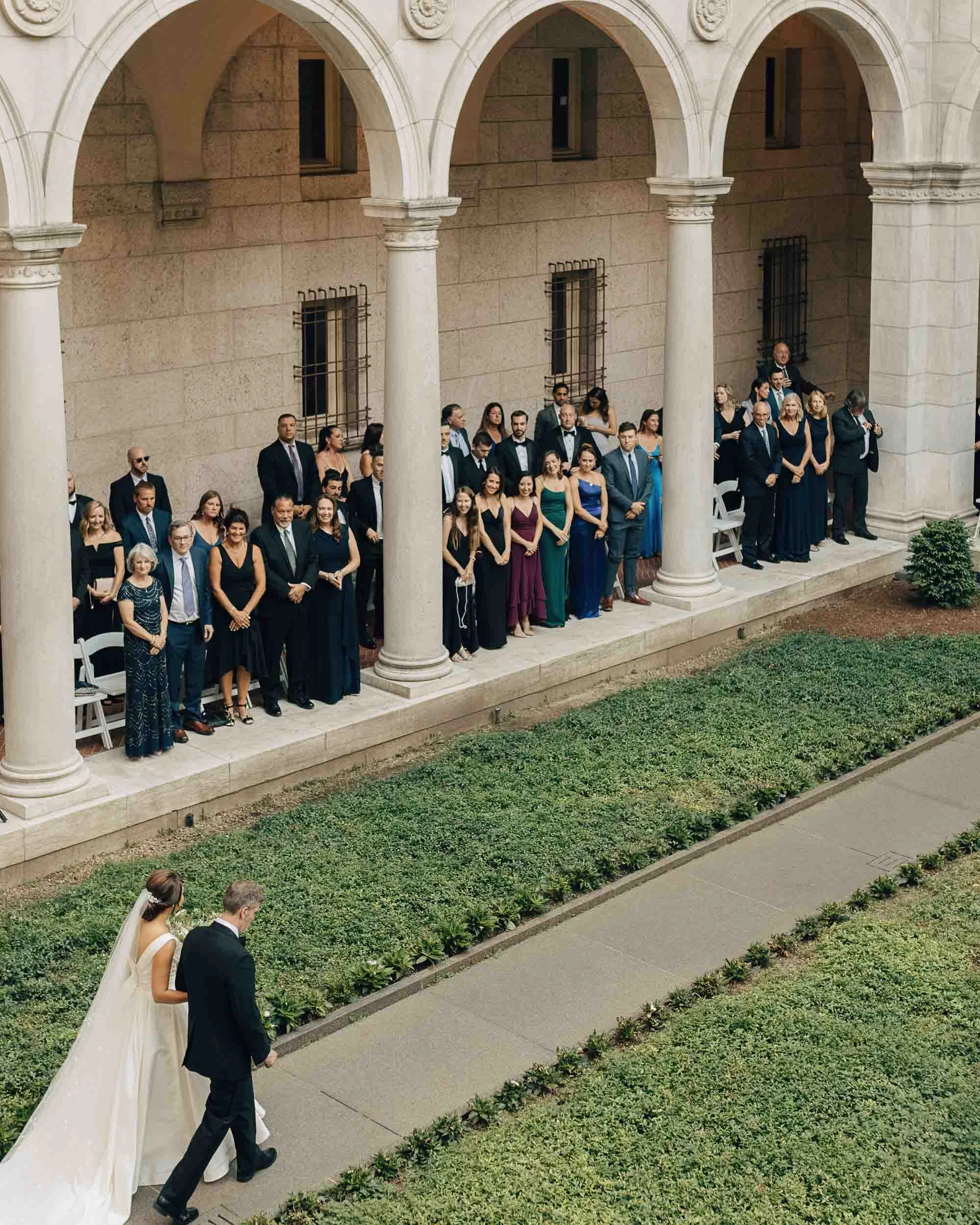 Guests standing in BPL colonnade as bride and groom walk down the aisle