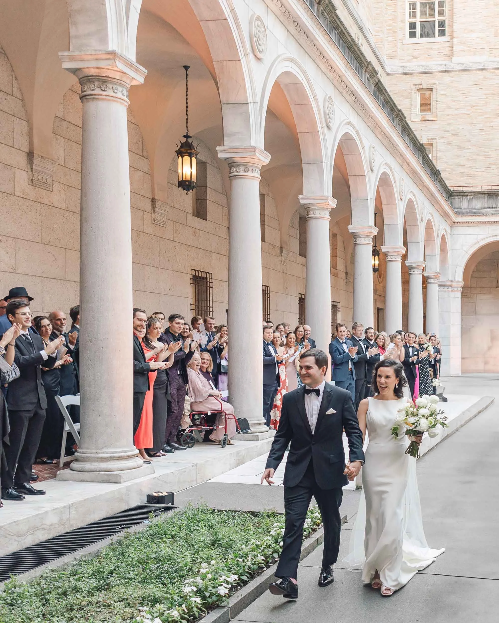 Newlyweds walking hand in hand through Boston Public Library courtyard.