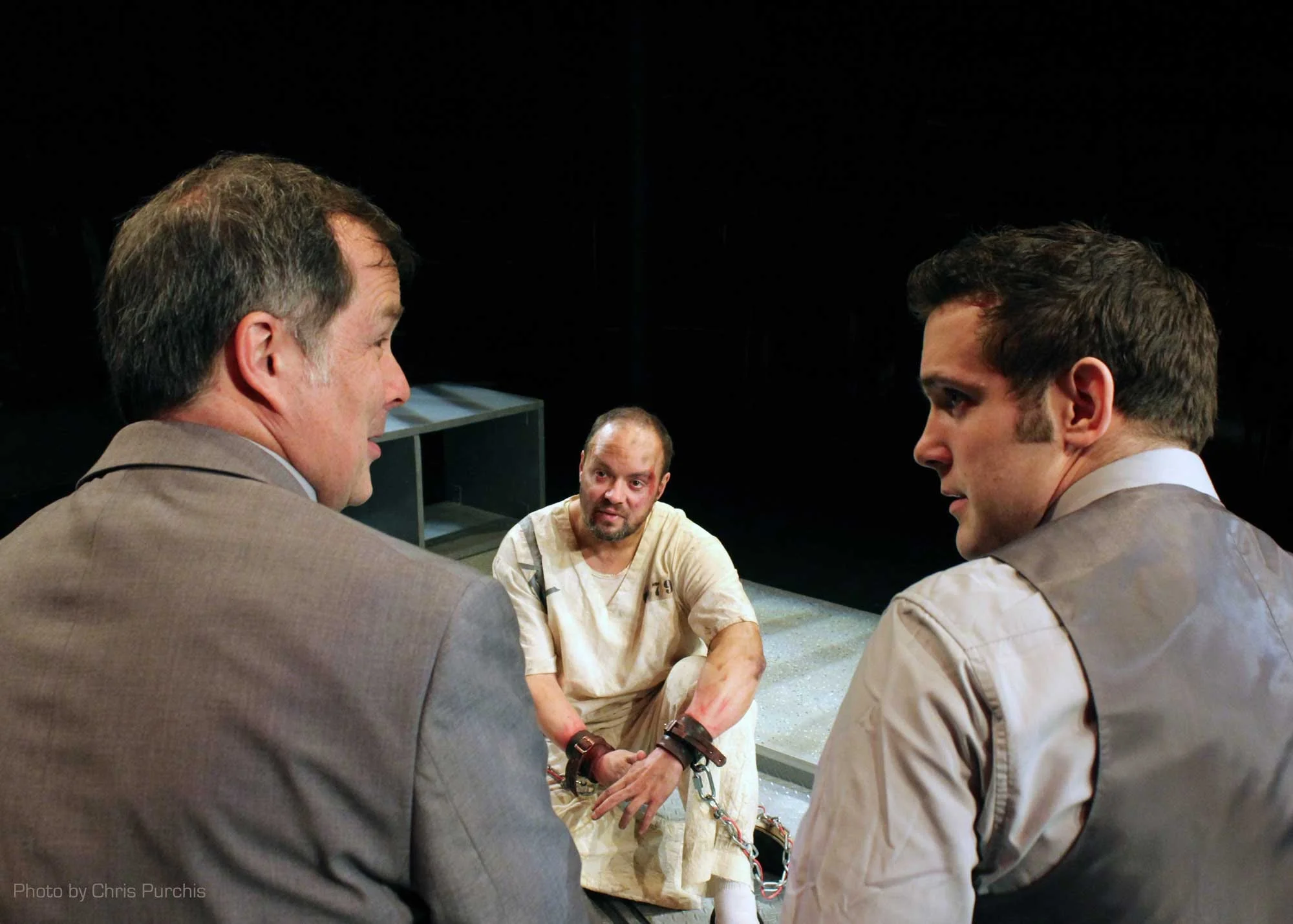" Wolber has a difficult task because his role is in such great contrast to everyone else on stage. Where they are stiff and unyielding, indistinguishable cogs in a machine, he is loose and human. He provides a contrast in posture, style of speech and depth of expression. He also must display intense physical pain and suffering. There is a moment where he rolls his eyes up so that only the whites of his eyes are displayed and he truly looks as though he is past the point of endurance." - EncoreMichigan
