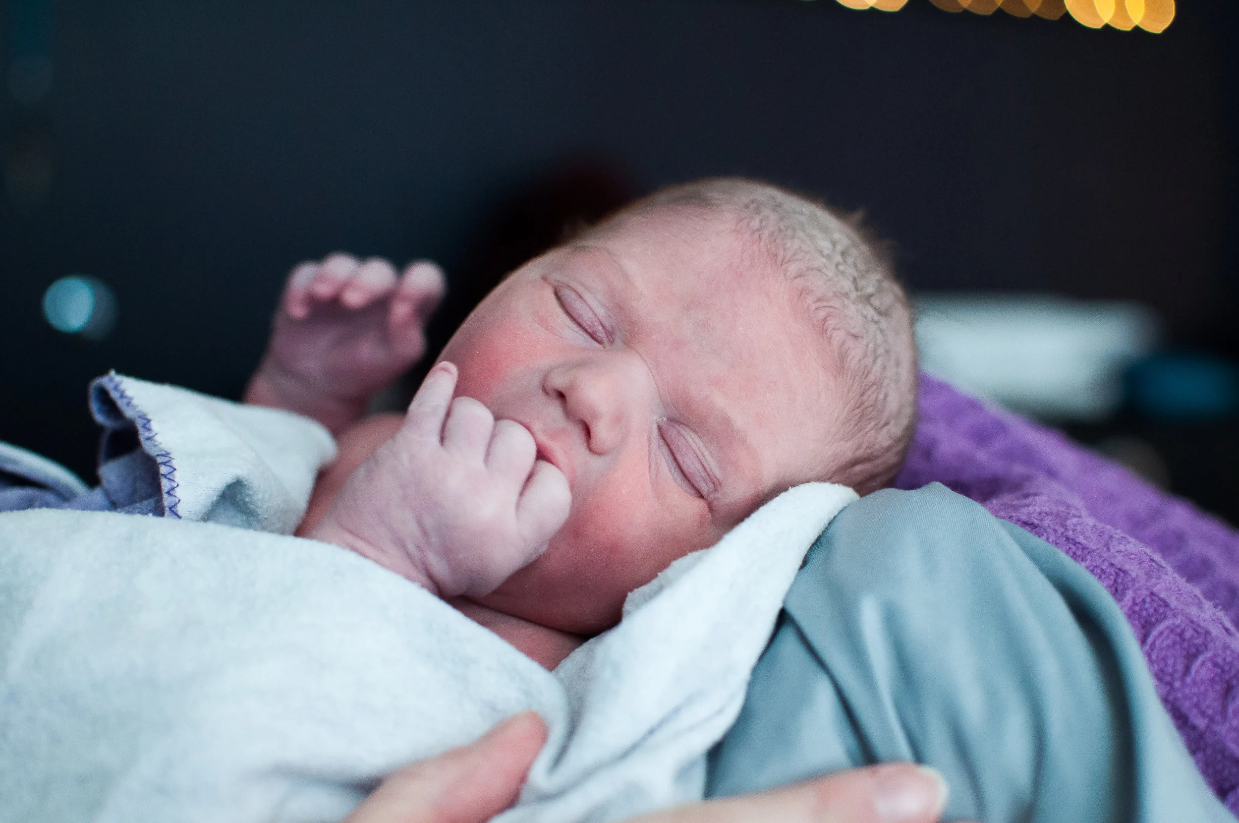 A newly born baby laying on a bare chest looking up at mother’s face offscreen.