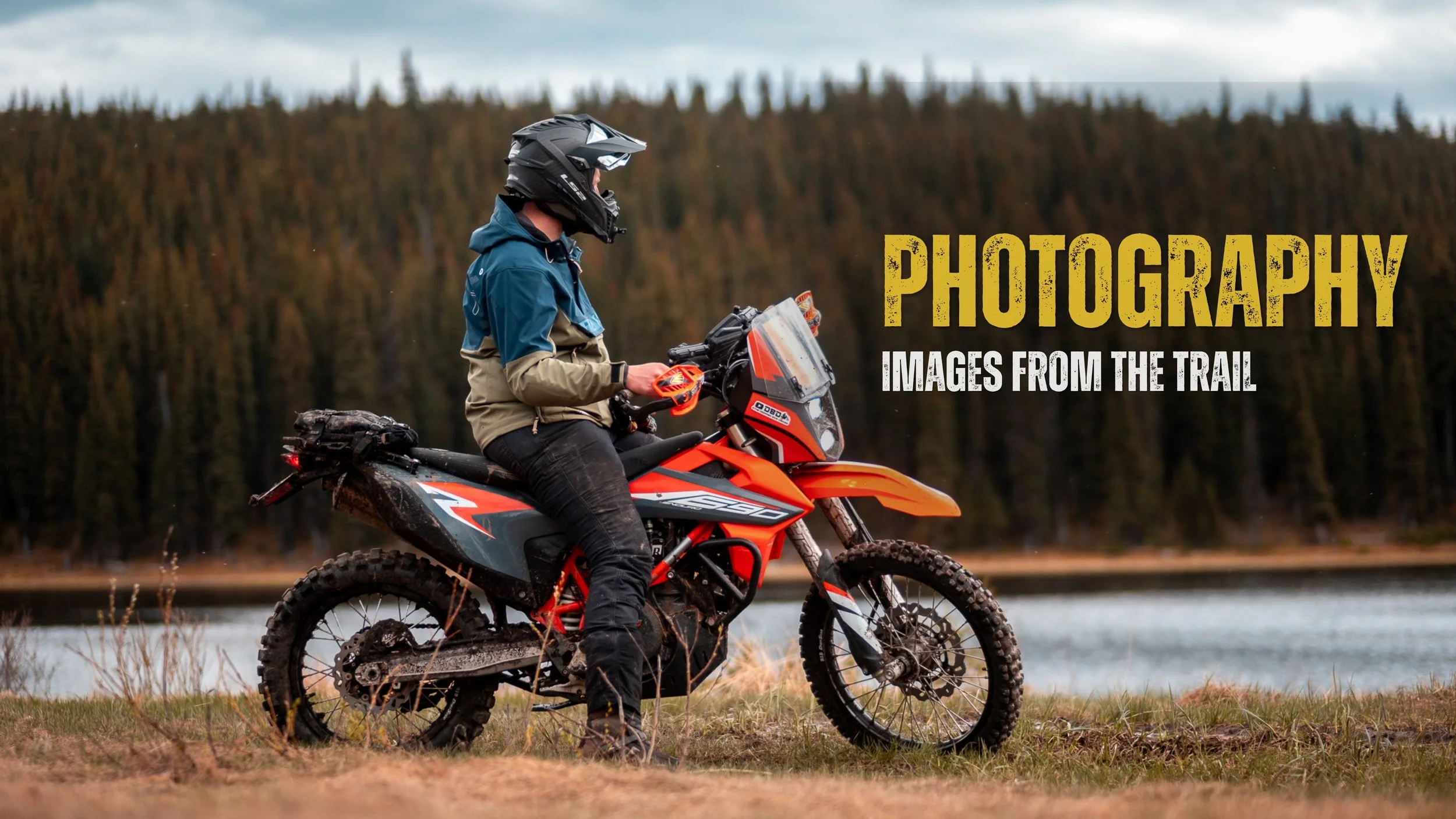 A person wearing a helmet and a blue and tan jacket riding an orange off-road motorcycle near a body of water with a forested background, with text that reads 'Photography - Images from the Trail'.