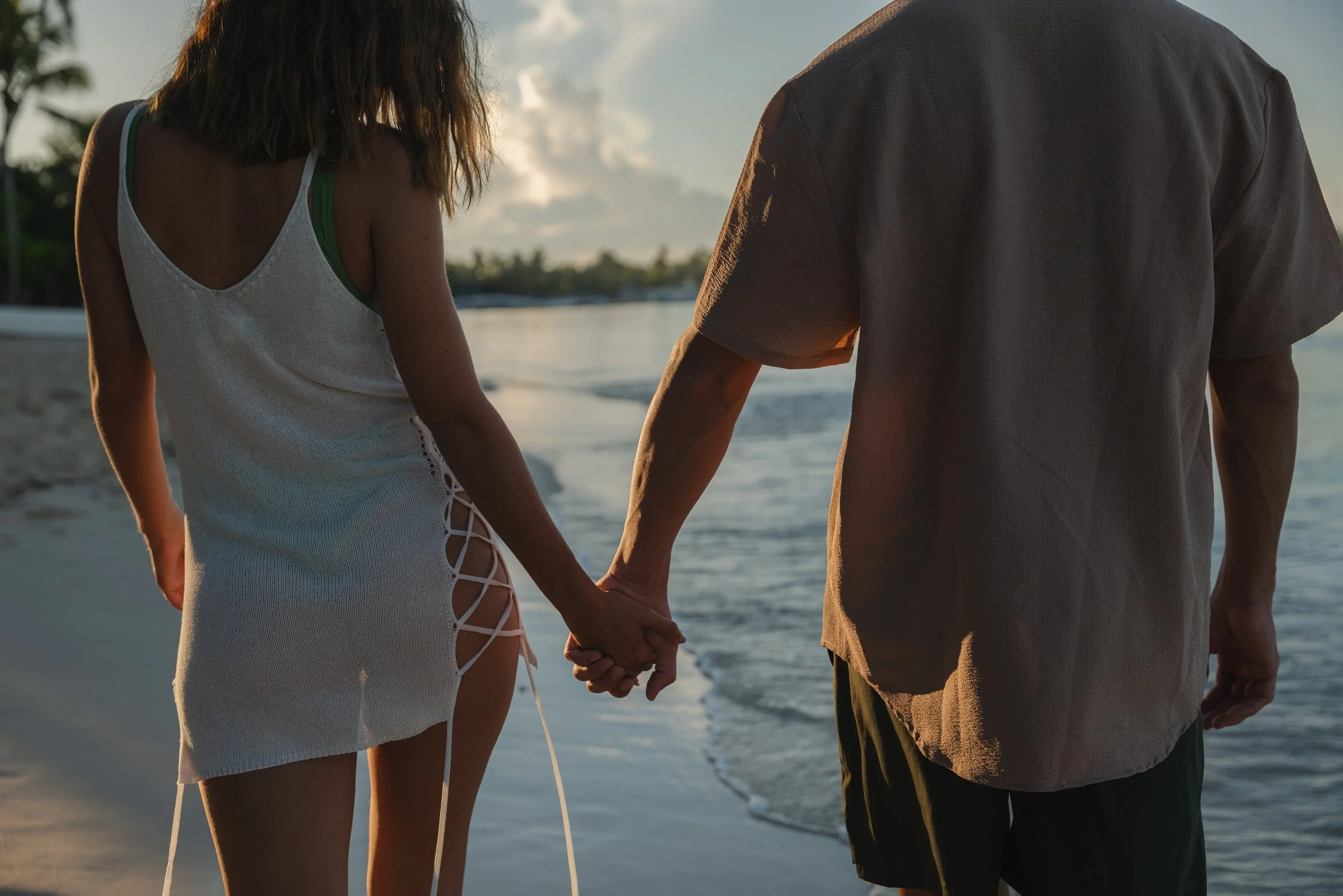Couple holding hands at sunset on the beach, luxury resort lifestyle photography by David McConaghy