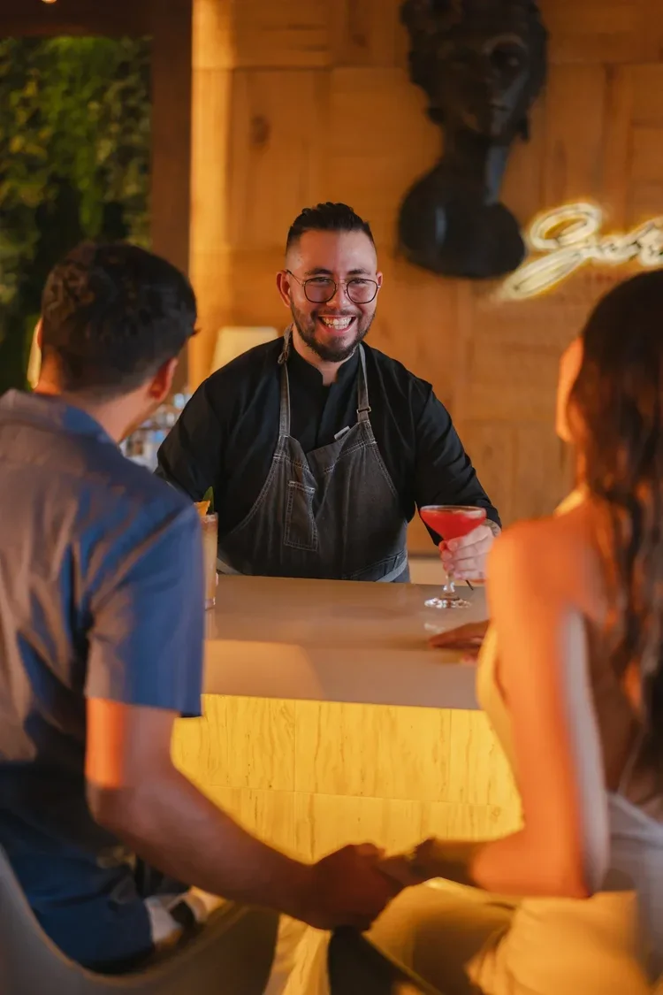 Hotel bartender serving cocktail to guests with smile, staff photography by David McConaghy