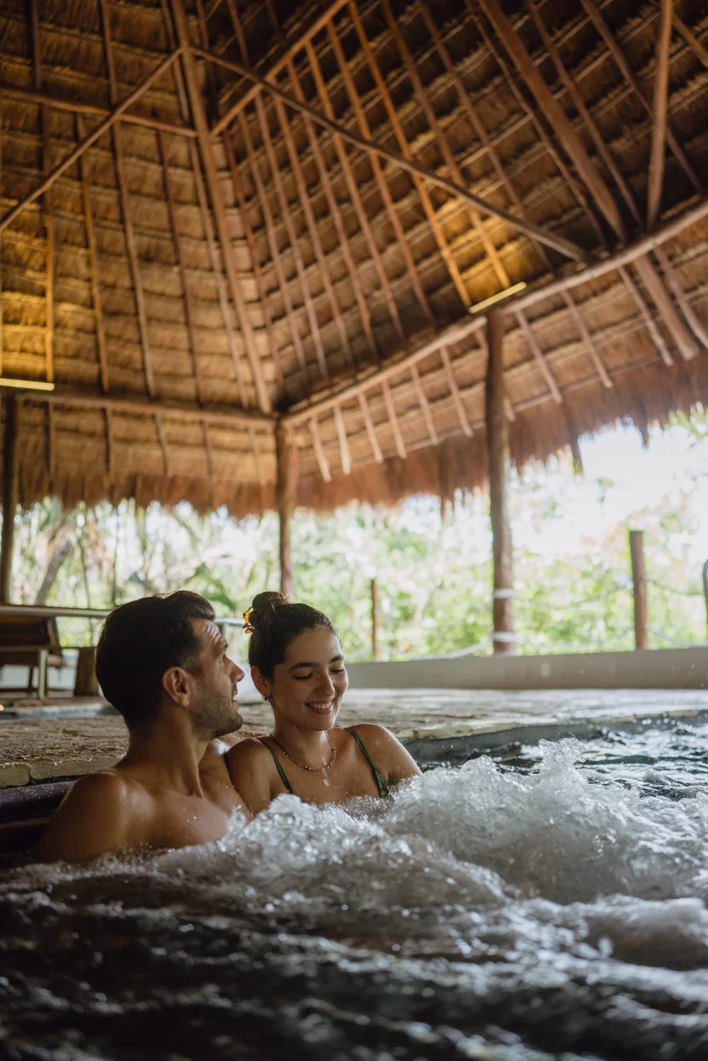 Couple relaxing in outdoor jacuzzi under thatched roof, spa photography by David McConaghy