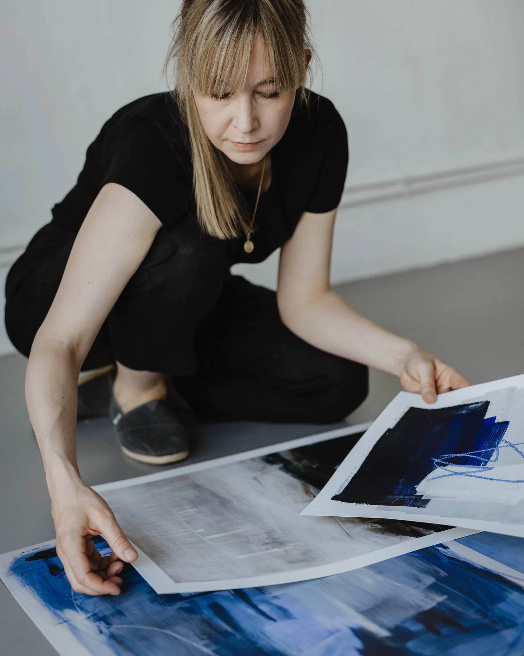 Artist Mareike Böhmer sitting on the floor of a gallery, looking at her exclusive art prints with blue and abstract designs.