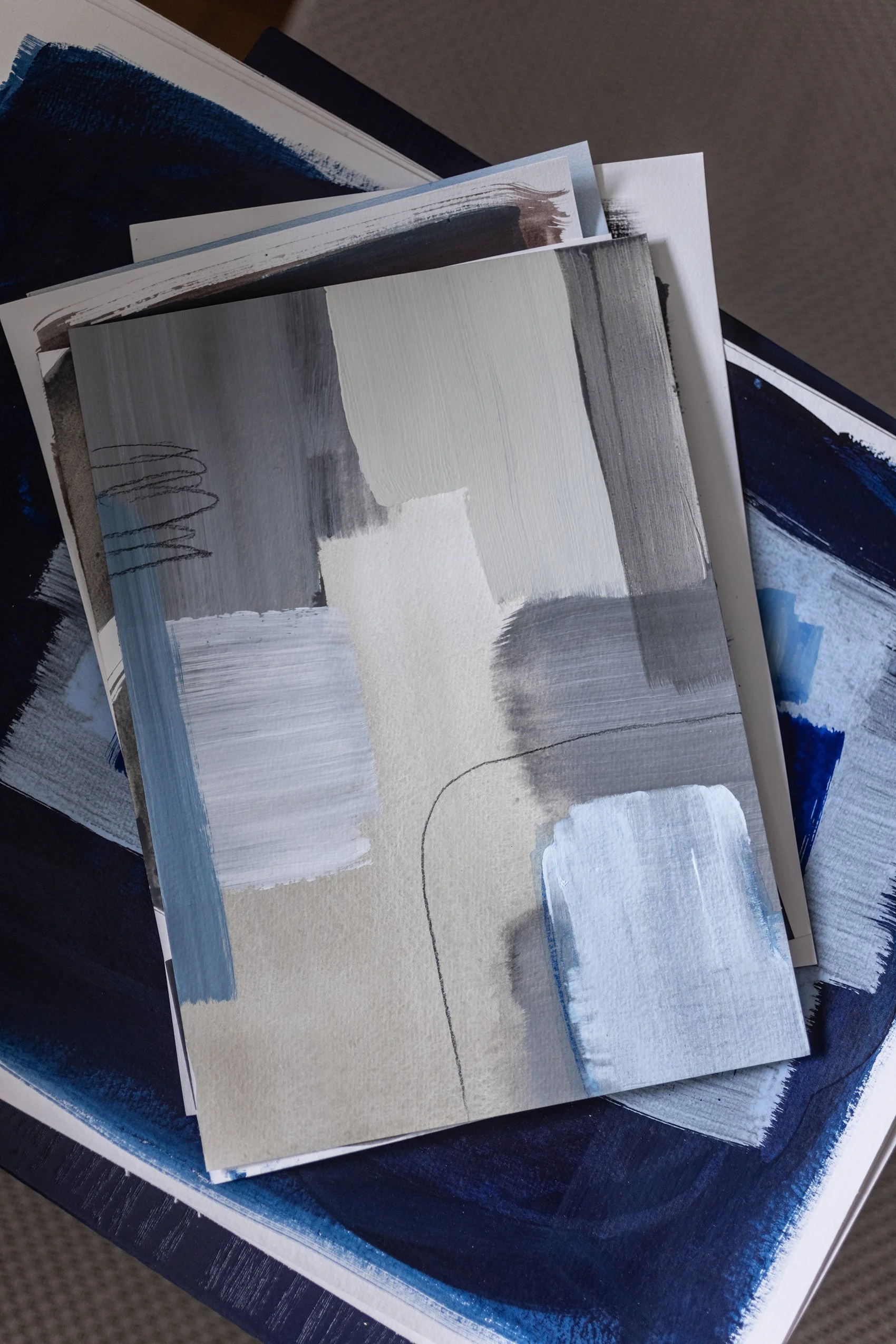Collection of abstract paintings with shades of black, white, gray, and blue, layered on a surface.