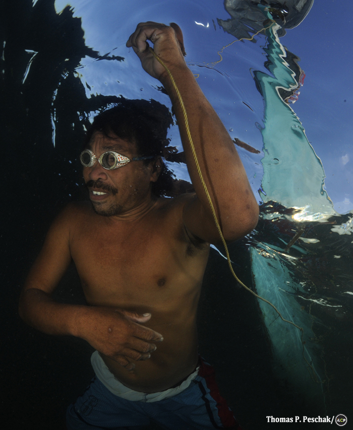 Swimming over a reef, a local lantern fisher pulls his boat behind him. Near handumon marine reserve, Danajon Bank.