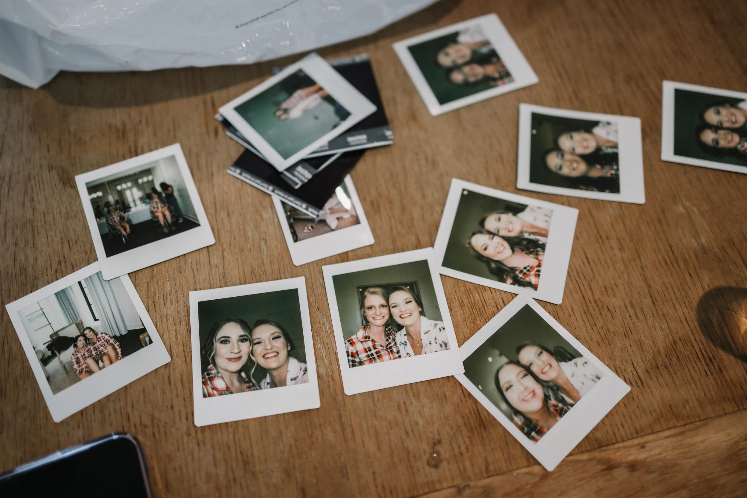 Scattered instant photographs of women smiling and posing, with some group shots, on a wooden table.