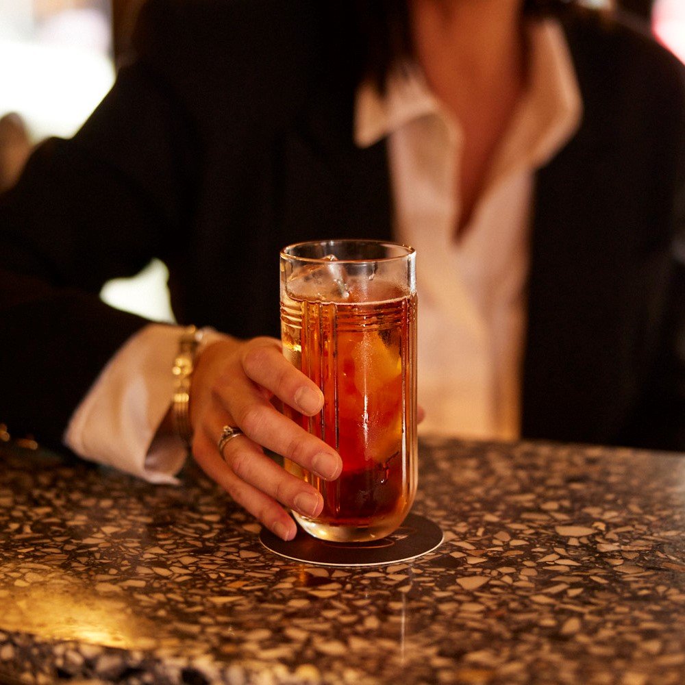 Womans hand holding an orange coloured  cocktail in a highball glass