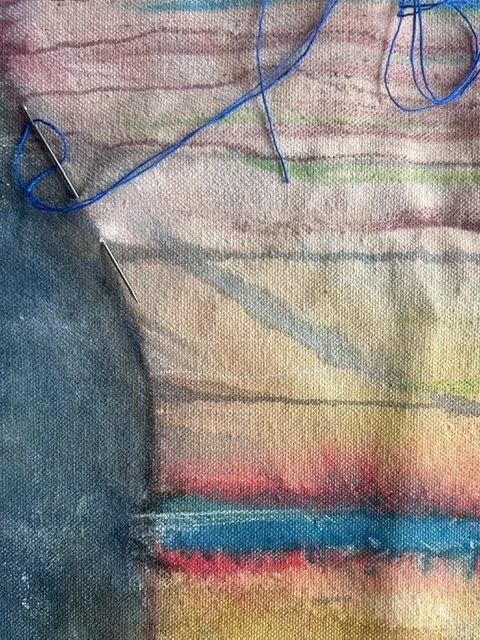 Close-up of colorful woven fabric with blue thread and sewing needles