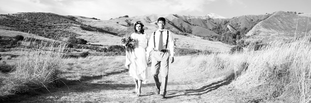 Bride and Groom Walking Hand-in-Hand with Flowers by Kate Healey