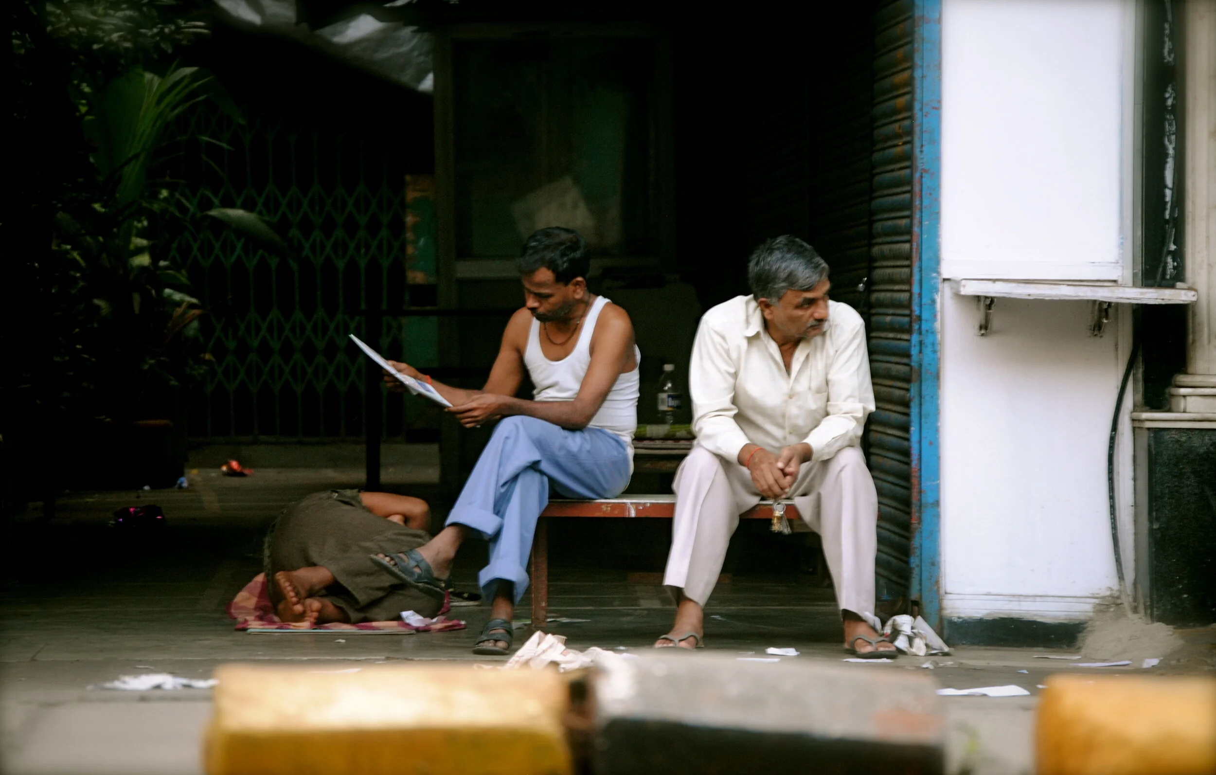   Bombay, India -  As one man naps another reads the morning news while the other stews in thought.  