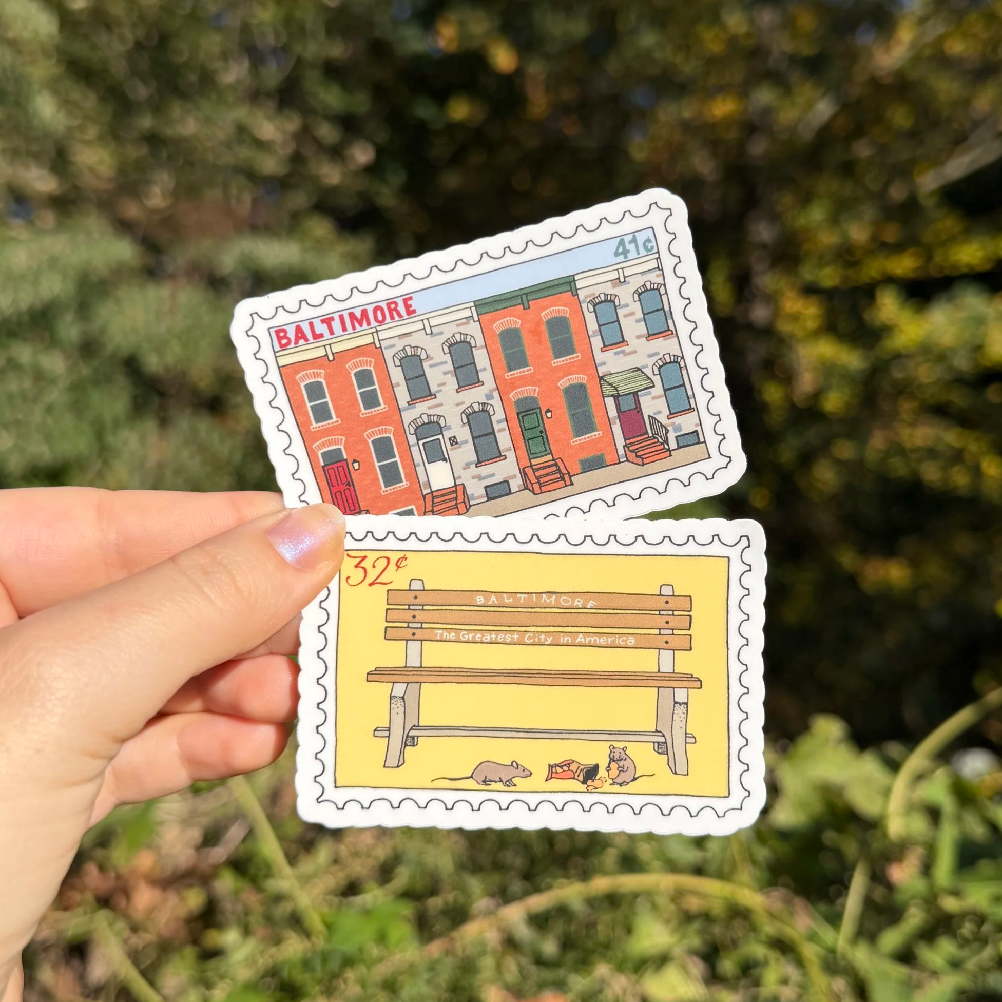 Two Baltimore-themed stamp stickers. One features illustration of Baltimore row houses and one features a "Greatest City in America" bench with rats eating chips
