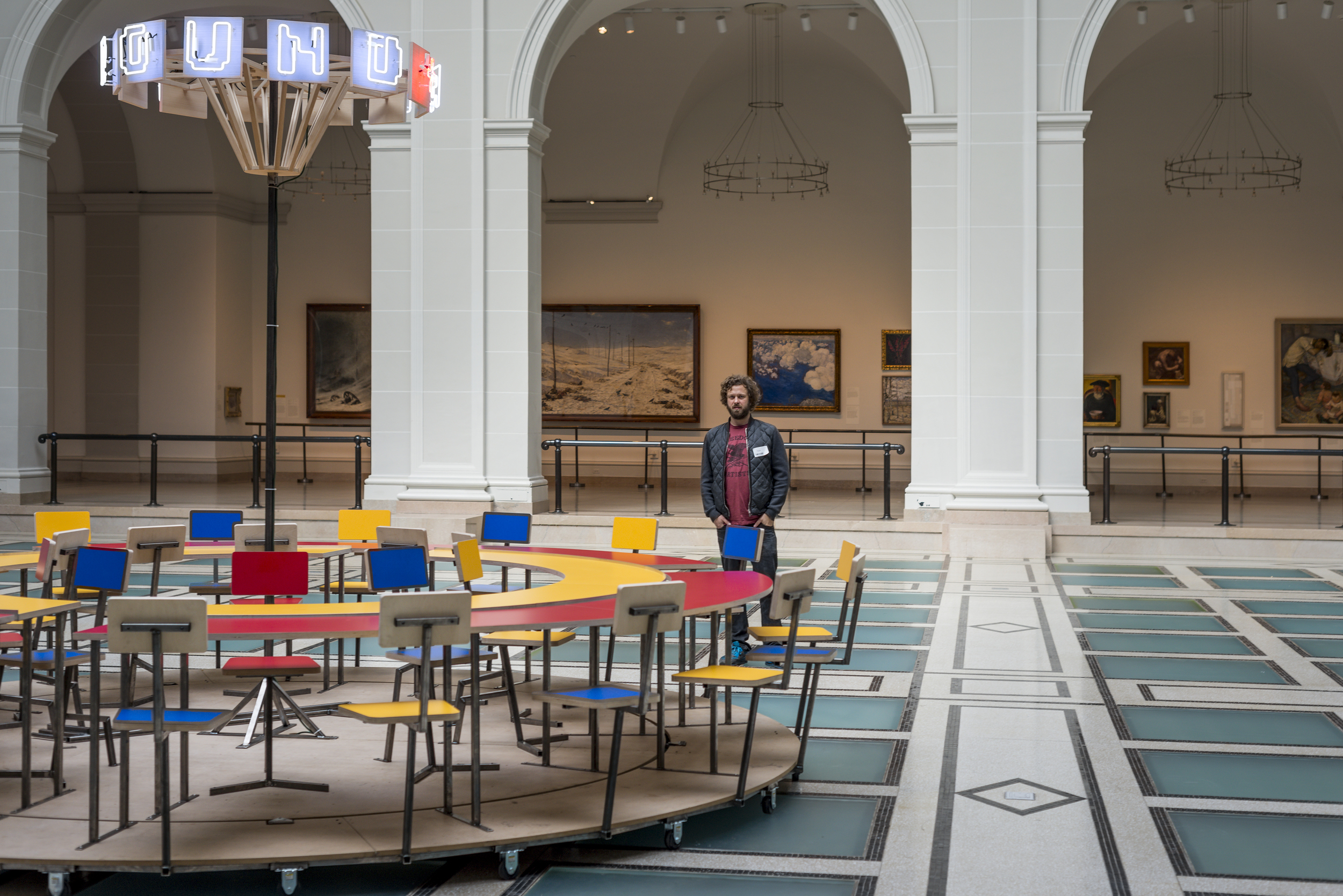  Oliver Clegg pictured with  Until the Cows Come Home  (2014), as installed at the Brooklyn Museum in 2014. Steel, neon, laminated mdf, pine; 60 x 168 in. (table), 24 x 60 in. (neon centerpiece). ( photo : Giles Ashford) 