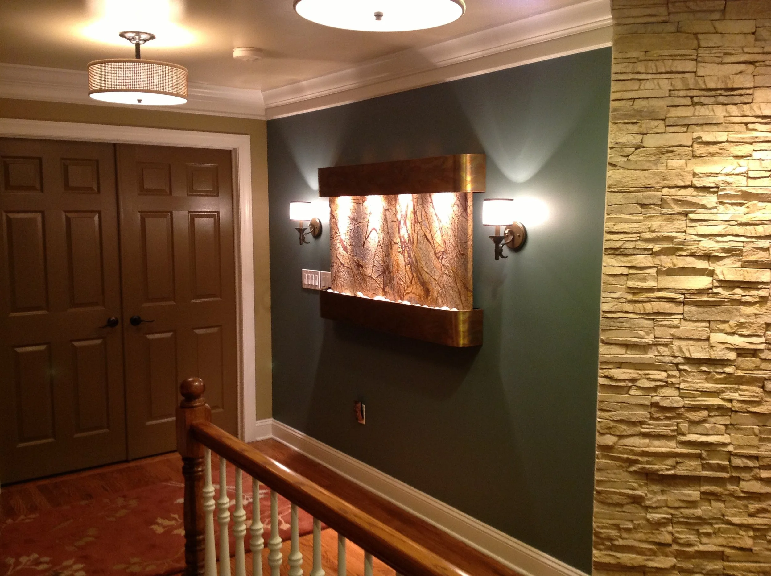 A thoughtfully designed hallway featuring walls and doors painted the same color, subtle semi-flush ceiling fixtures, and a custom wall-mounted waterfall fountain that creates a calming transition between rooms.