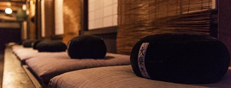 Image description: a row of zafus and zabutons in a warmly lit room