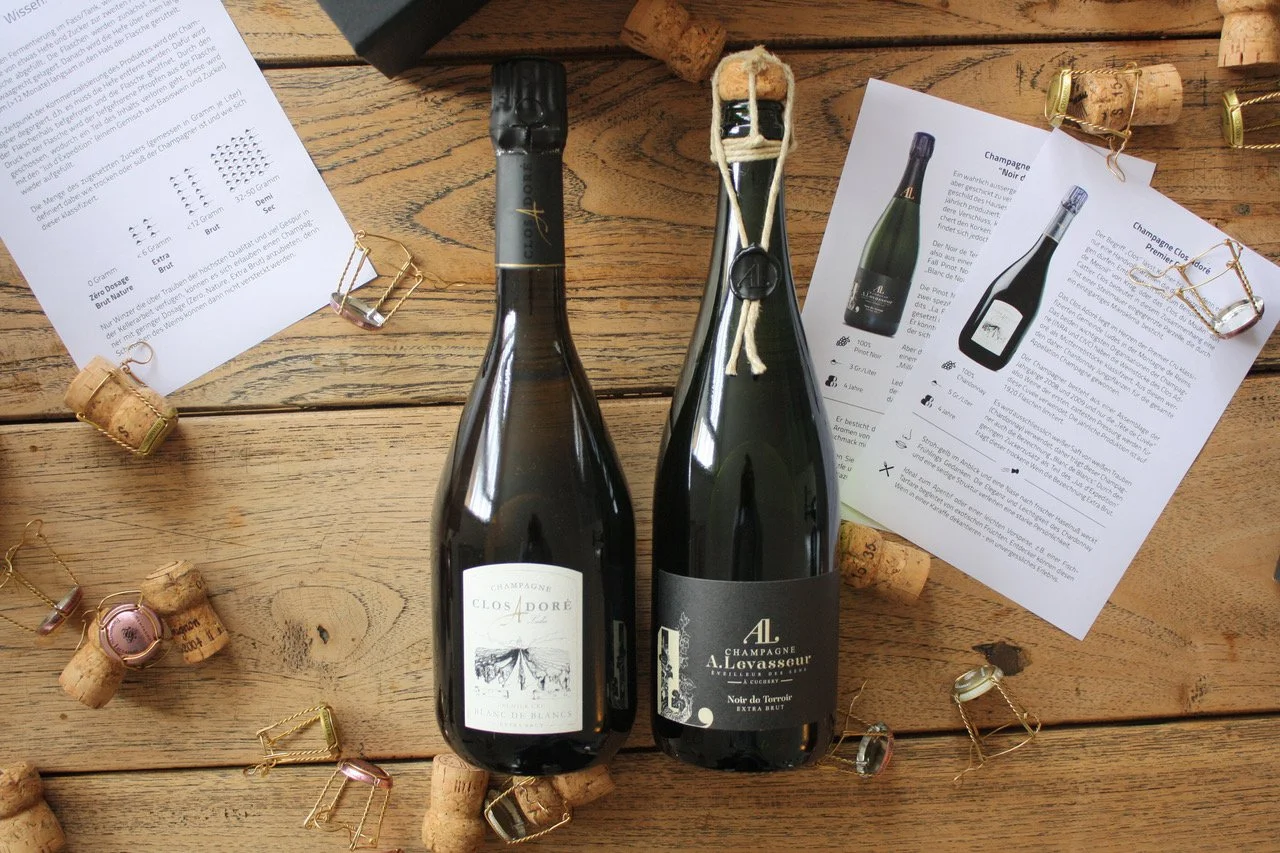 Zwei Champagnerflaschen auf einem Holztisch umgeben von Champagnerkorken und ausgedruckten Beschreibungen zu den Champagnern