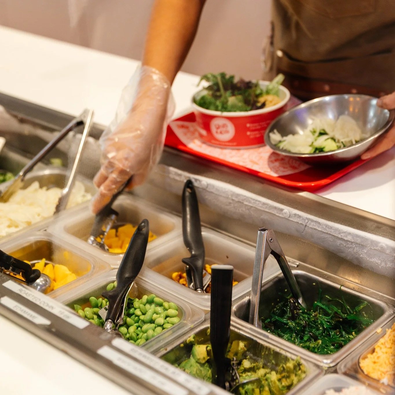 Uroko Poke line server preparing a poke bowl at the ingredient station